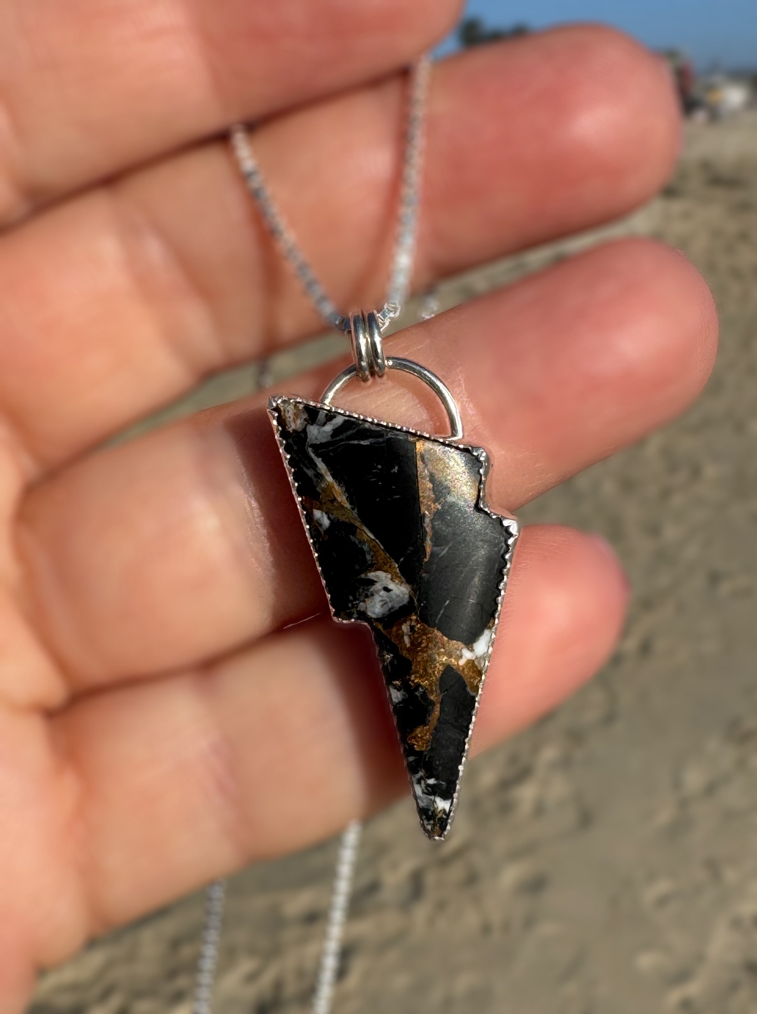 Lightning bolt-shaped pendant with black and bronze and white buffalo design held by a hand against a blurred background