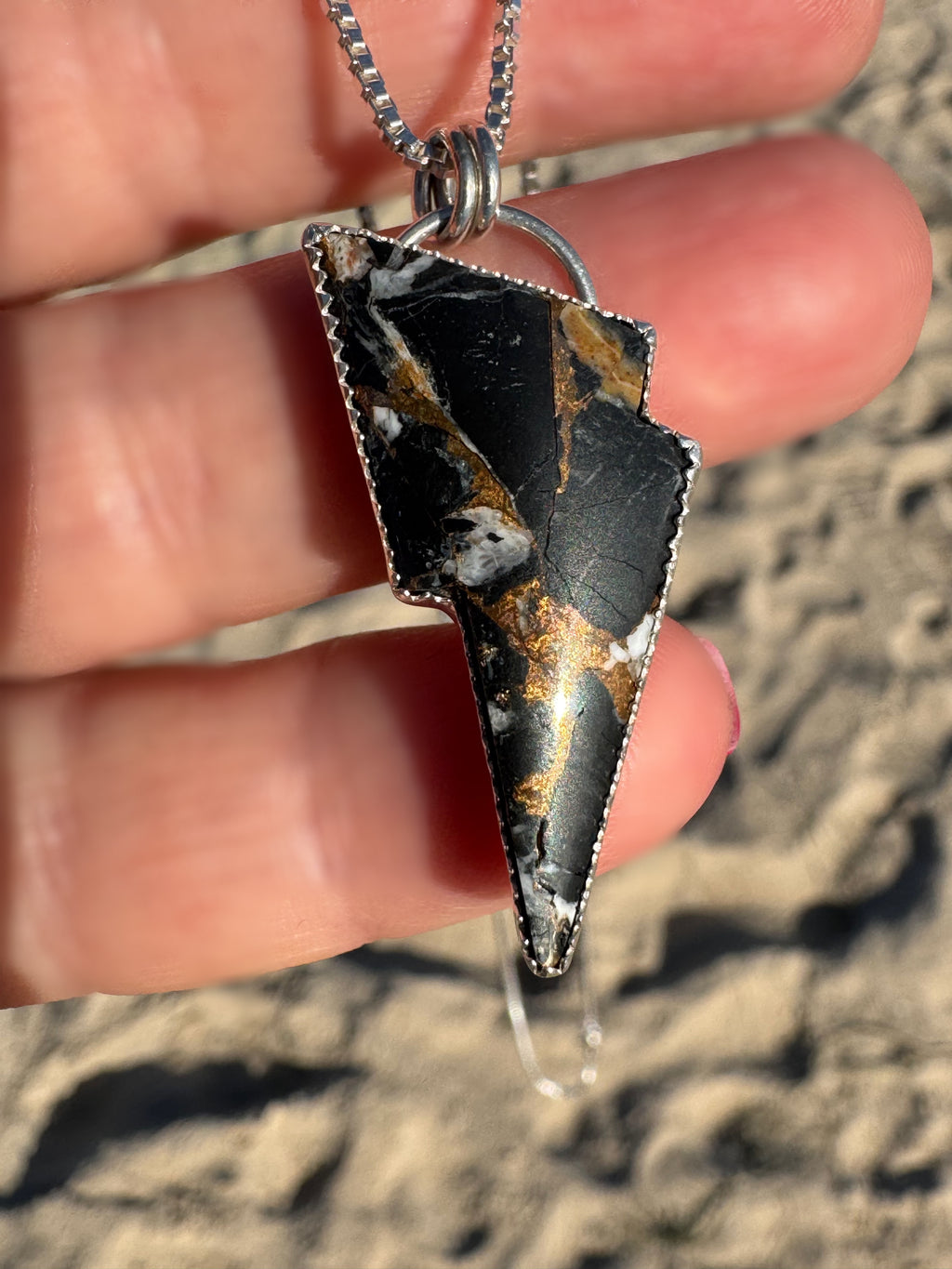 Pendant with a black and bronze/gold design held by a hand against a sandy background