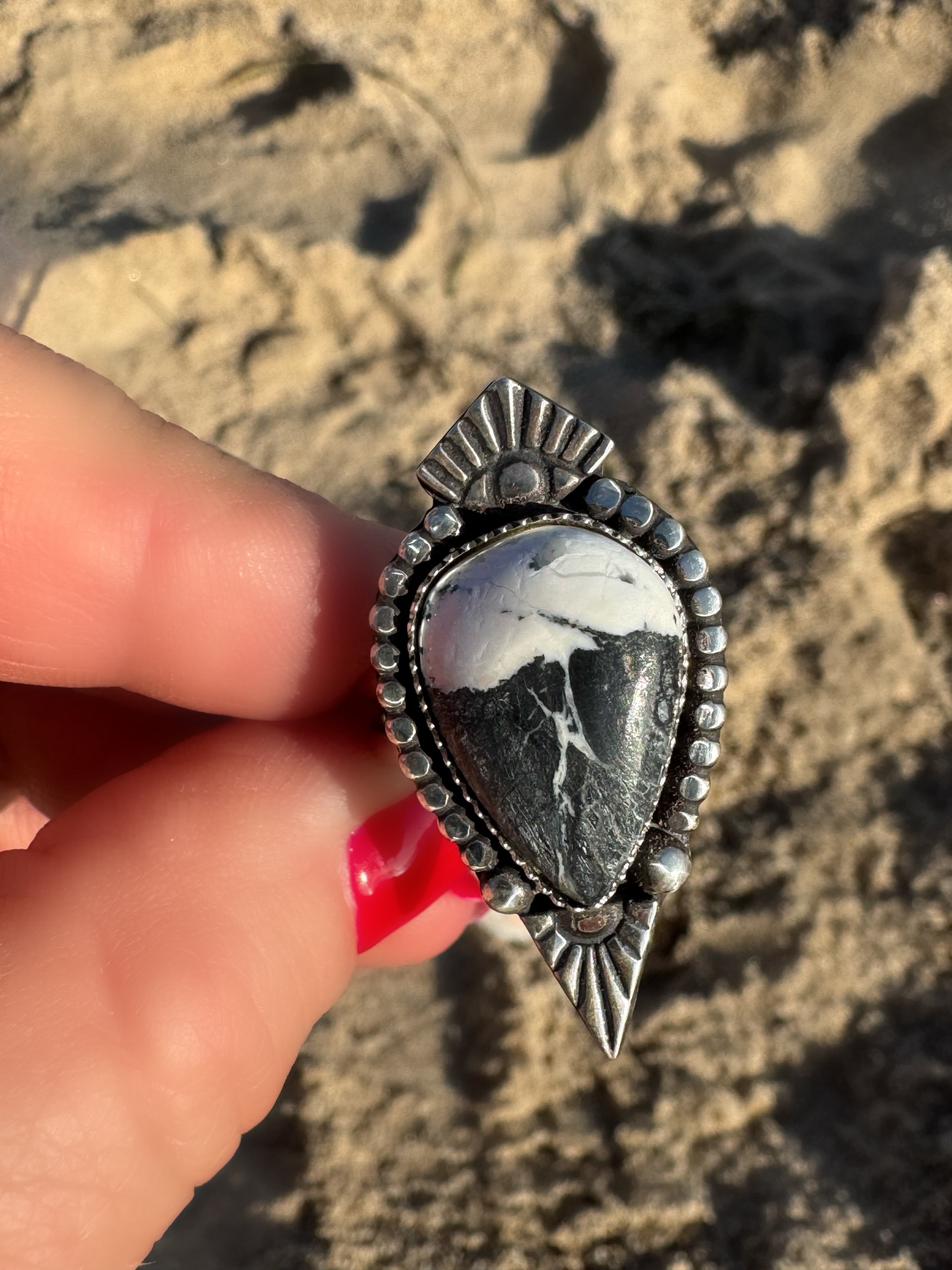 Silver ring with a stone held by a hand against a sandy background
