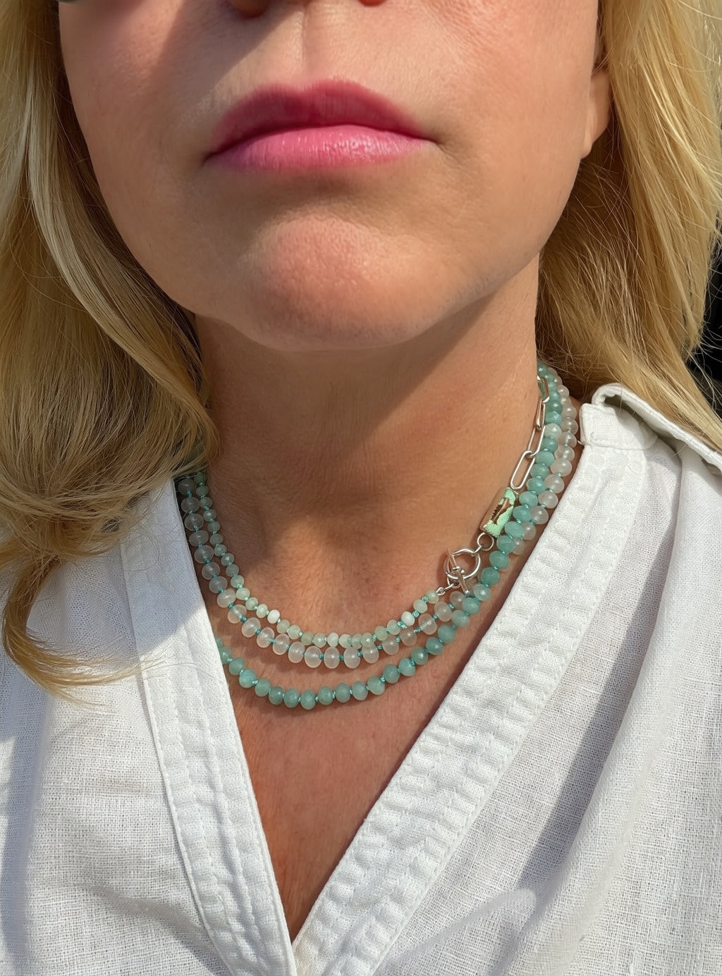 Close-up of a woman wearing layered necklaces with Caribbean blue, mint green and white beads, a silver paperclip chain, and a sterling toggle closure.