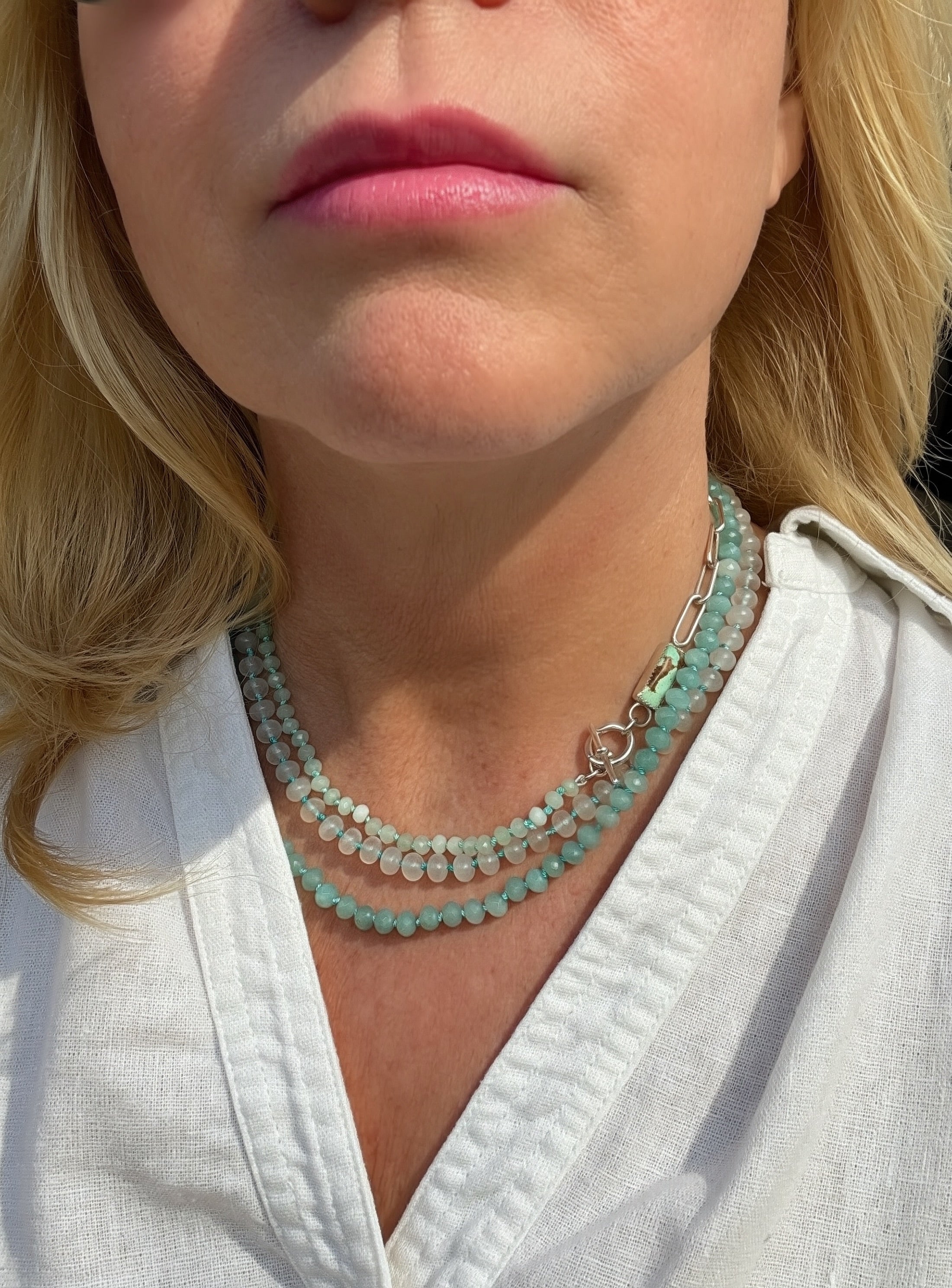 Close-up of a woman wearing layered necklaces with Caribbean blue, mint green and white beads, a silver paperclip chain, and a sterling toggle closure.