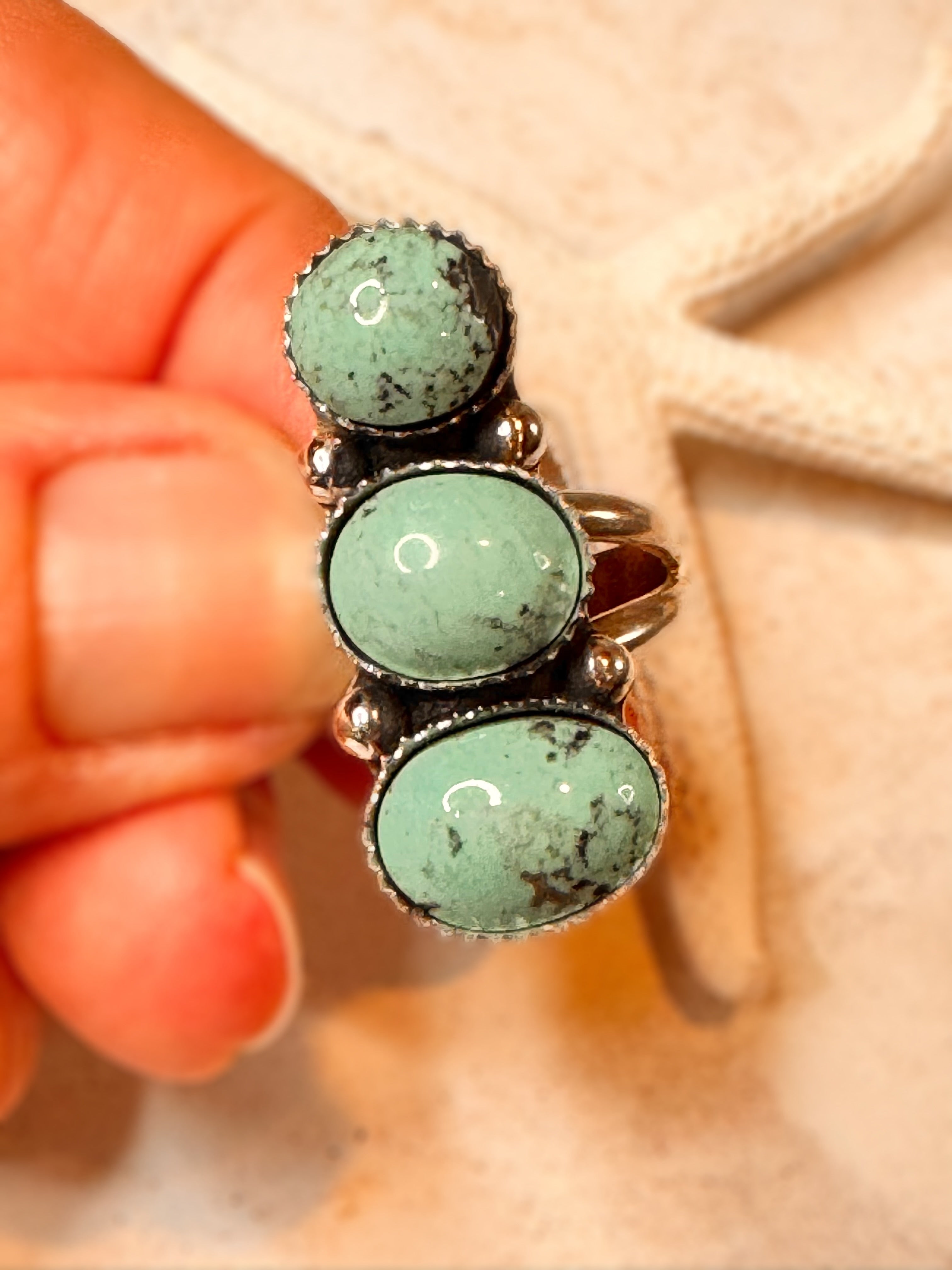 Turquoise stone ring held by a hand against a beige background