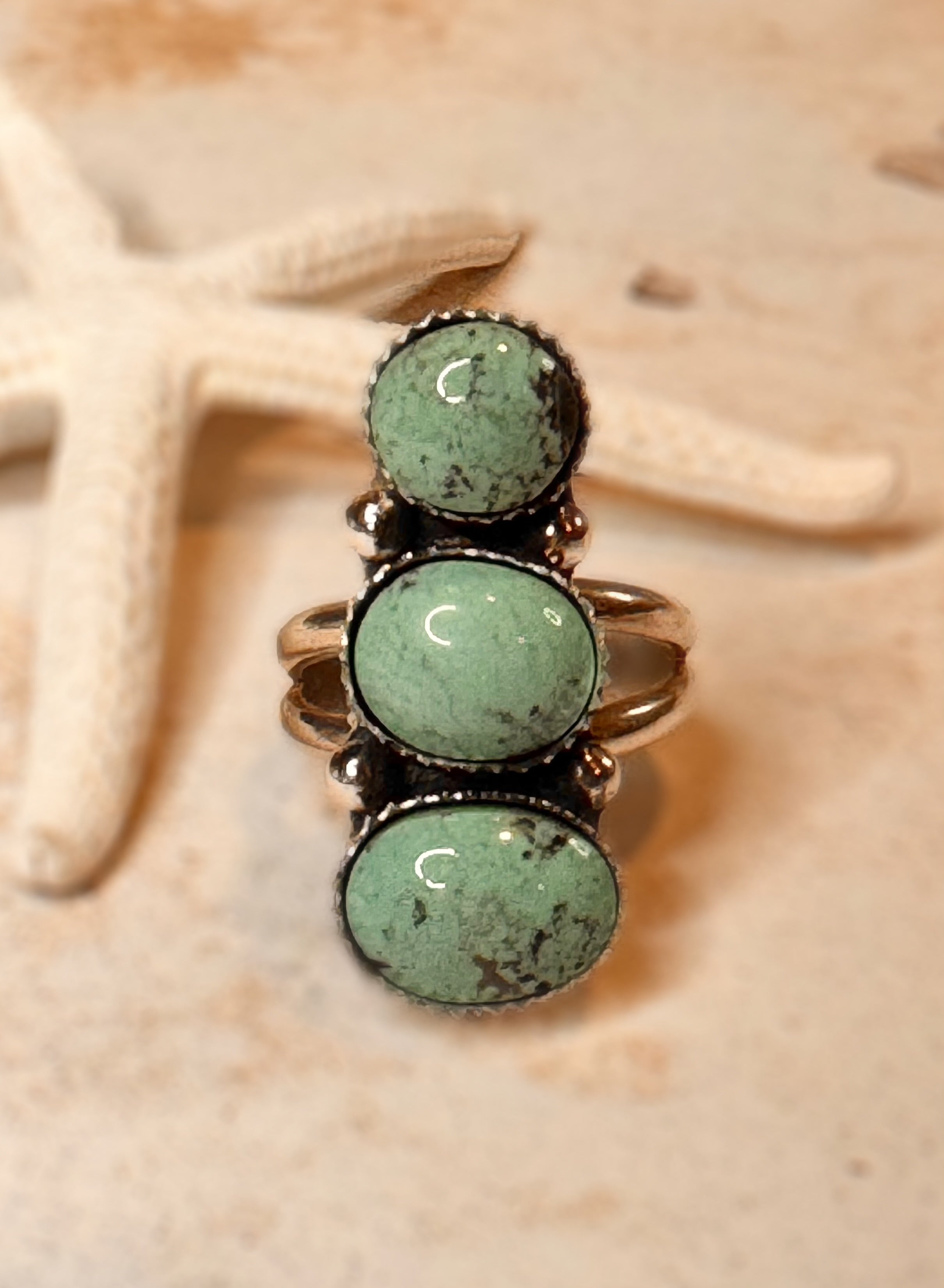 Ring with three green gemstones on a beige starfish background