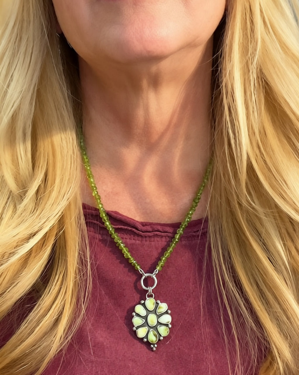 Verdant Sun necklace worn with a plum top, showing the peridot strand and sunburst pendant scale.