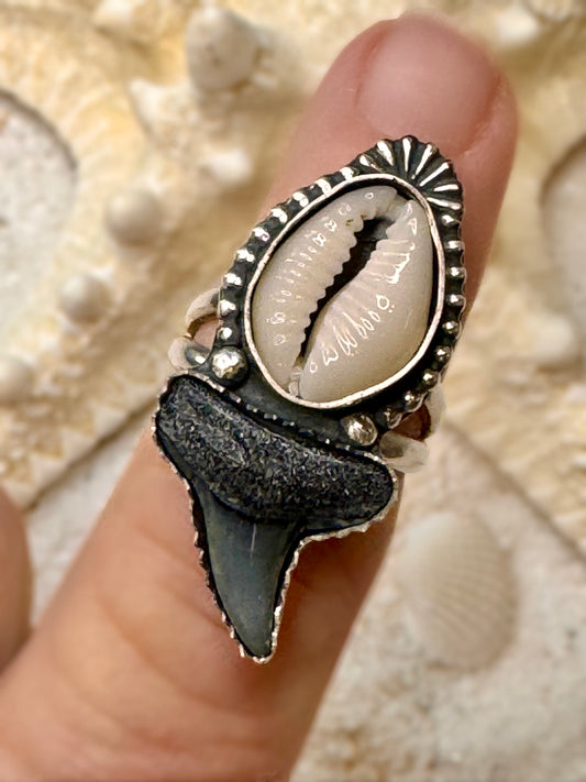 Ring with shark tooth and shell design on a finger against a shell background