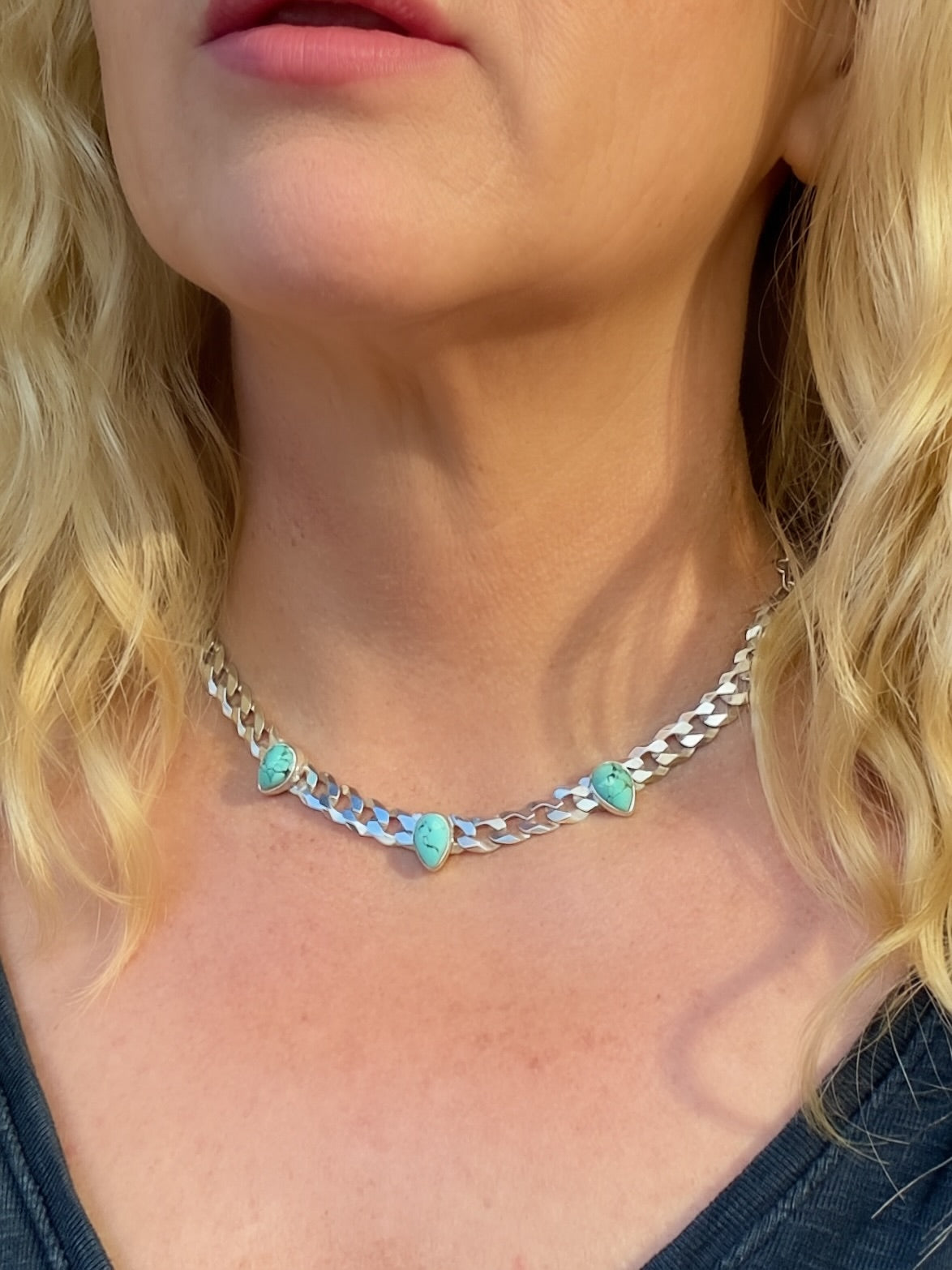 Three-stone turquoise necklace worn with a dark top, showing its short length and polished silver chain.