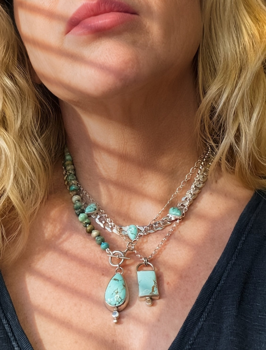 Blue Reign turquoise chain necklace layered with separate beaded and pendant necklaces over a dark top.