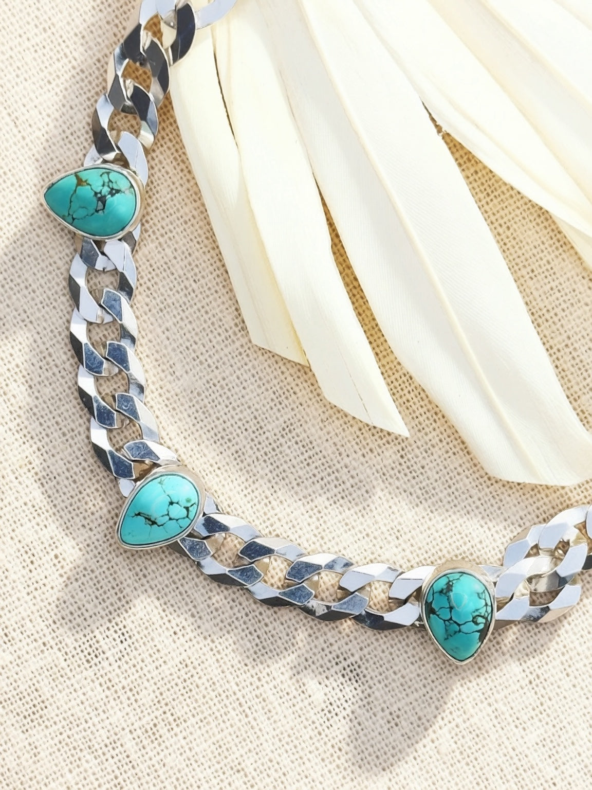 Blue Reign turquoise necklace on cream fabric, showing three teardrop stones set along polished sterling silver curb chain.