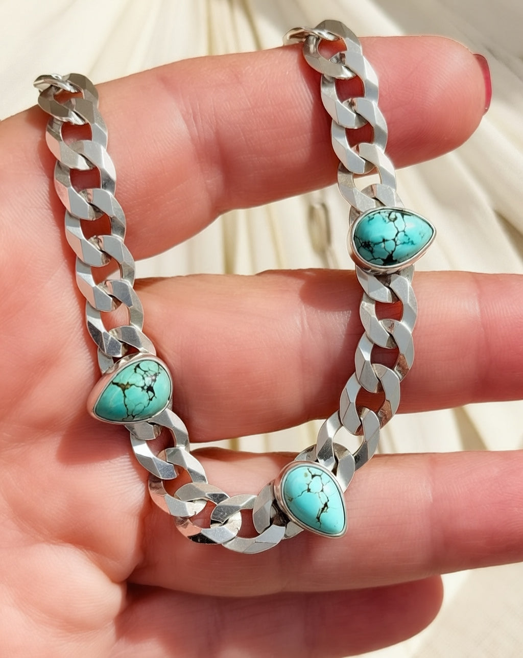 Blue Reign necklace held across fingers, showing turquoise matrix, smooth silver bezels, and broad curb links.