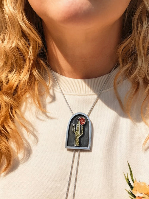 Person wearing a silver bolo necklace with a pendant featuring a saguaro in peridot and sun in goldstone.