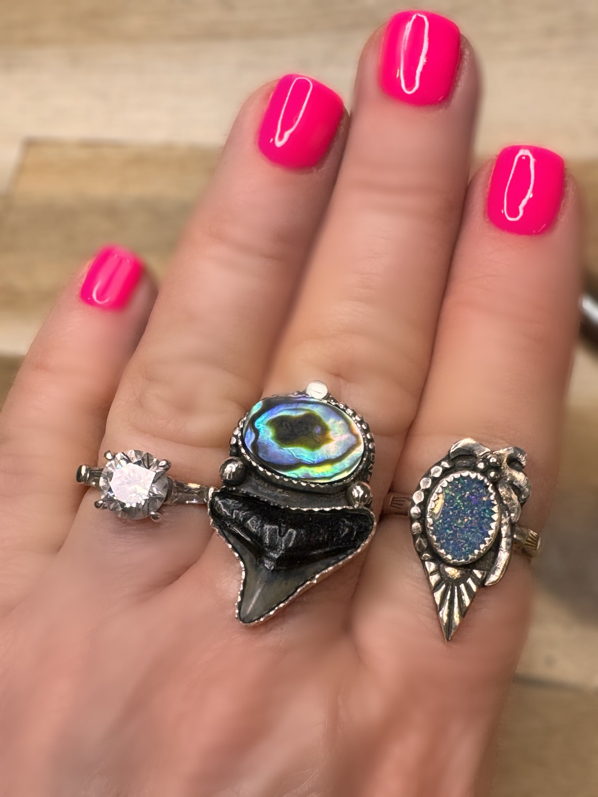 Abalone shell and shark tooth ring on a hand with pink nail polish on a neutral background