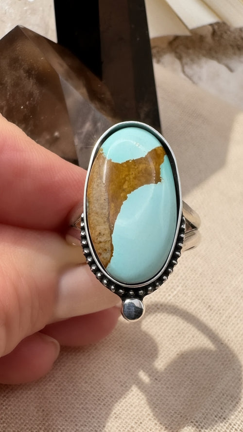 Ring with a turquoise stone held by a hand on a textured surface