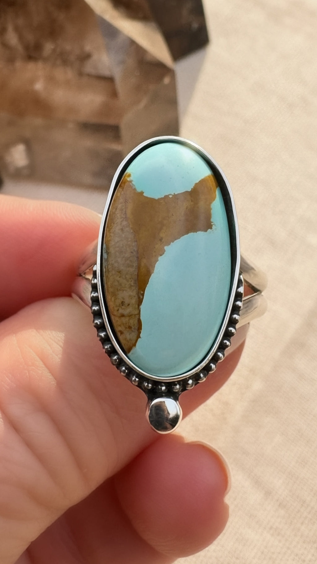 Turquoise stone and silver ring held in a hand against a neutral background