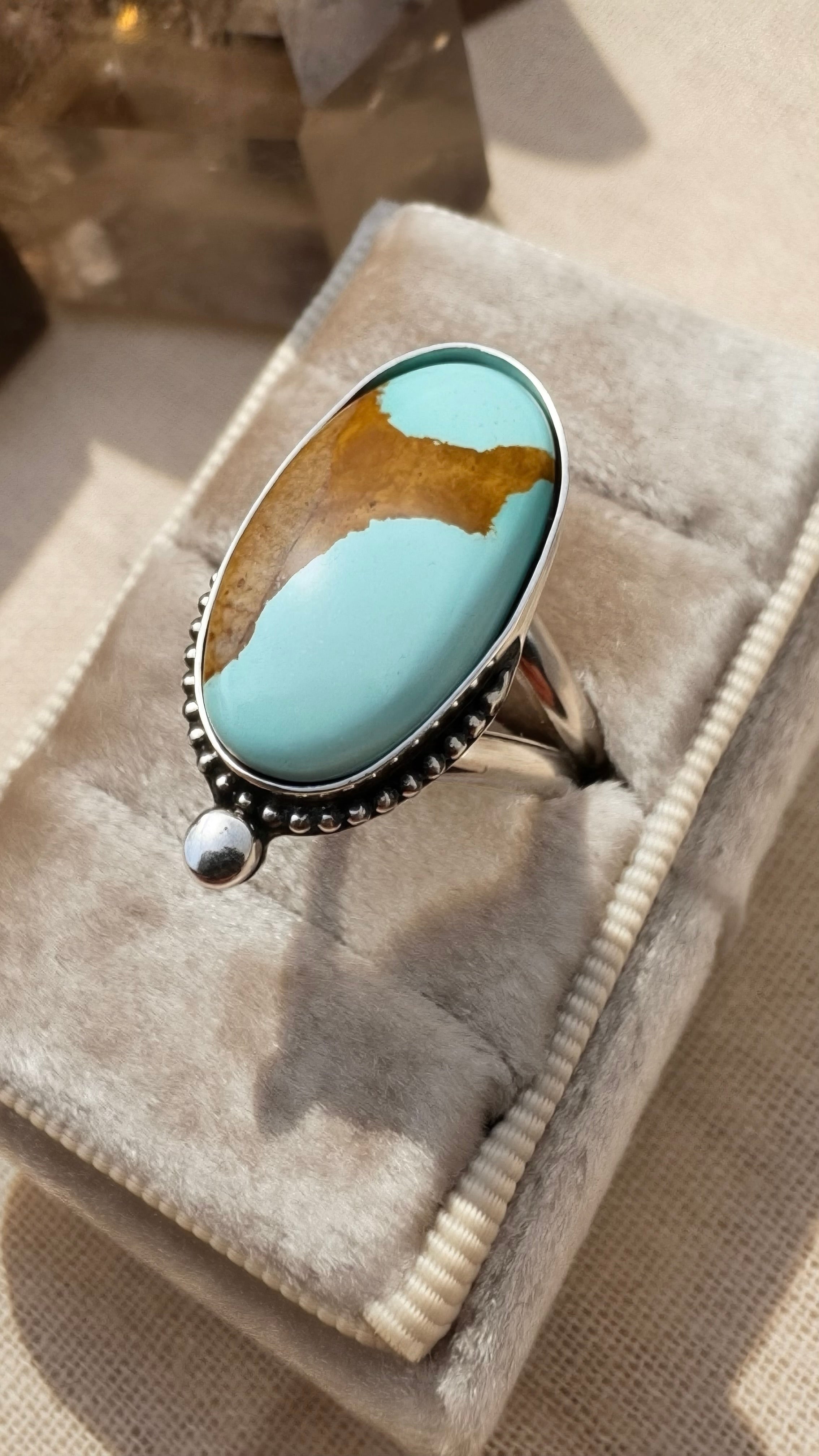 Turquoise stone ring on a gray velvet cushion