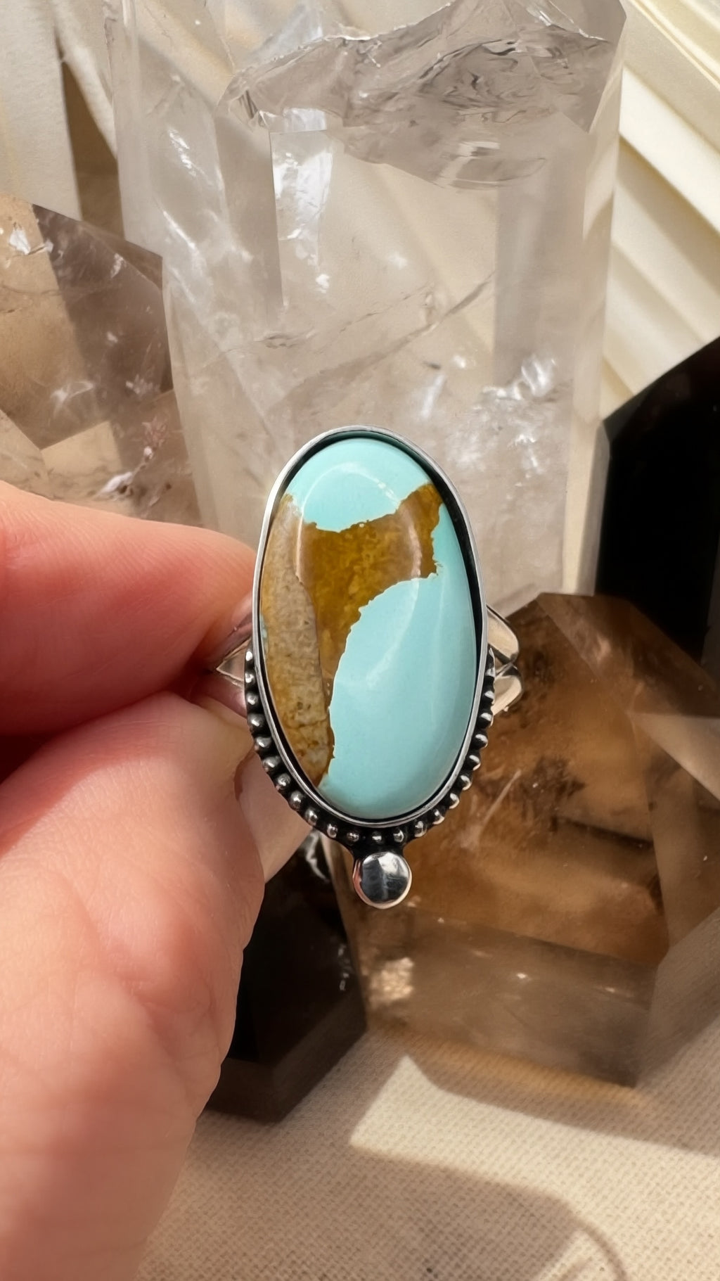 Turquoise stone ring held by a hand with a crystal background