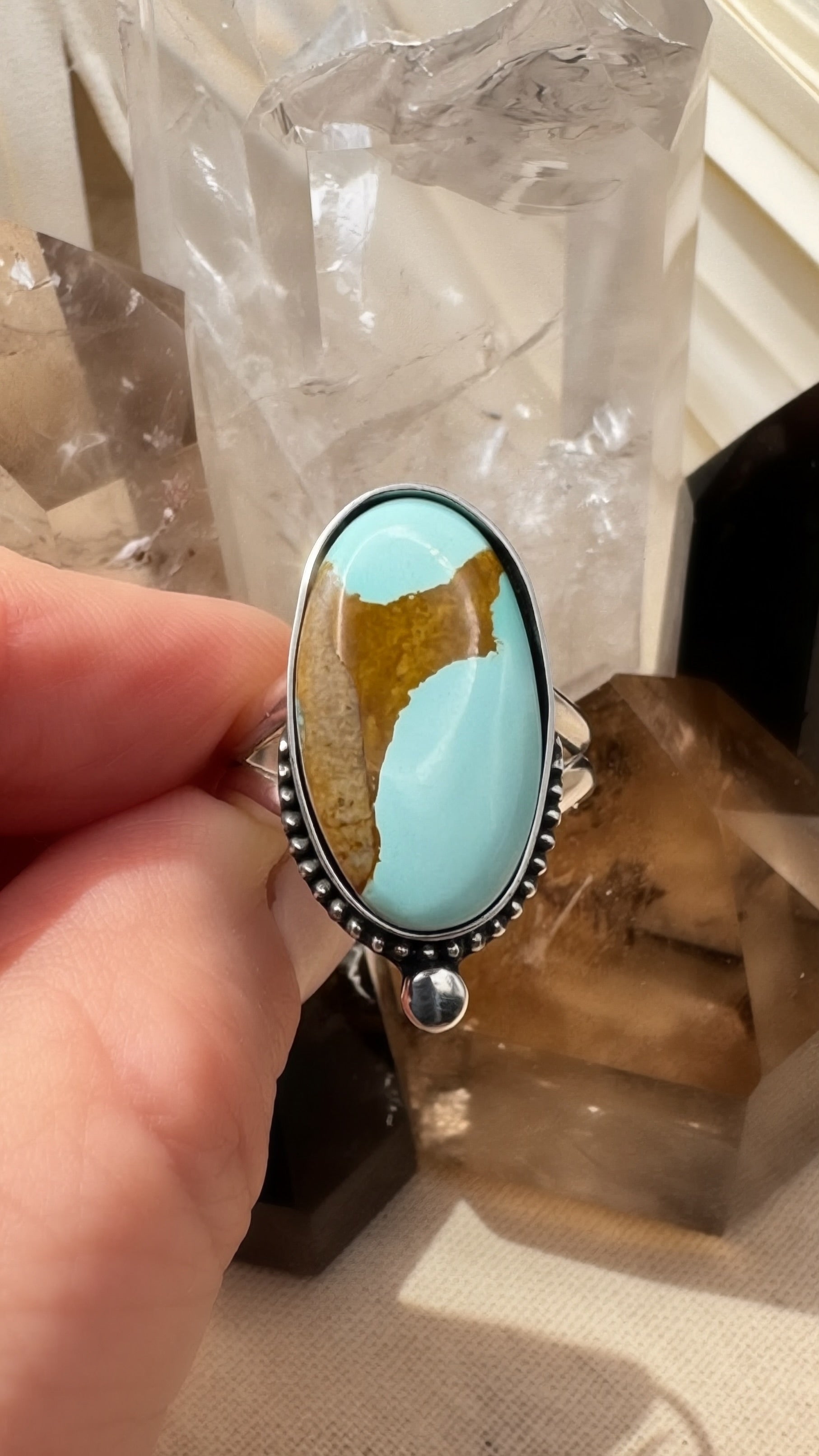 Turquoise stone ring held by a hand with a crystal background