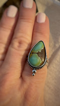 Turquoise ring on a person's finger with a neutral background