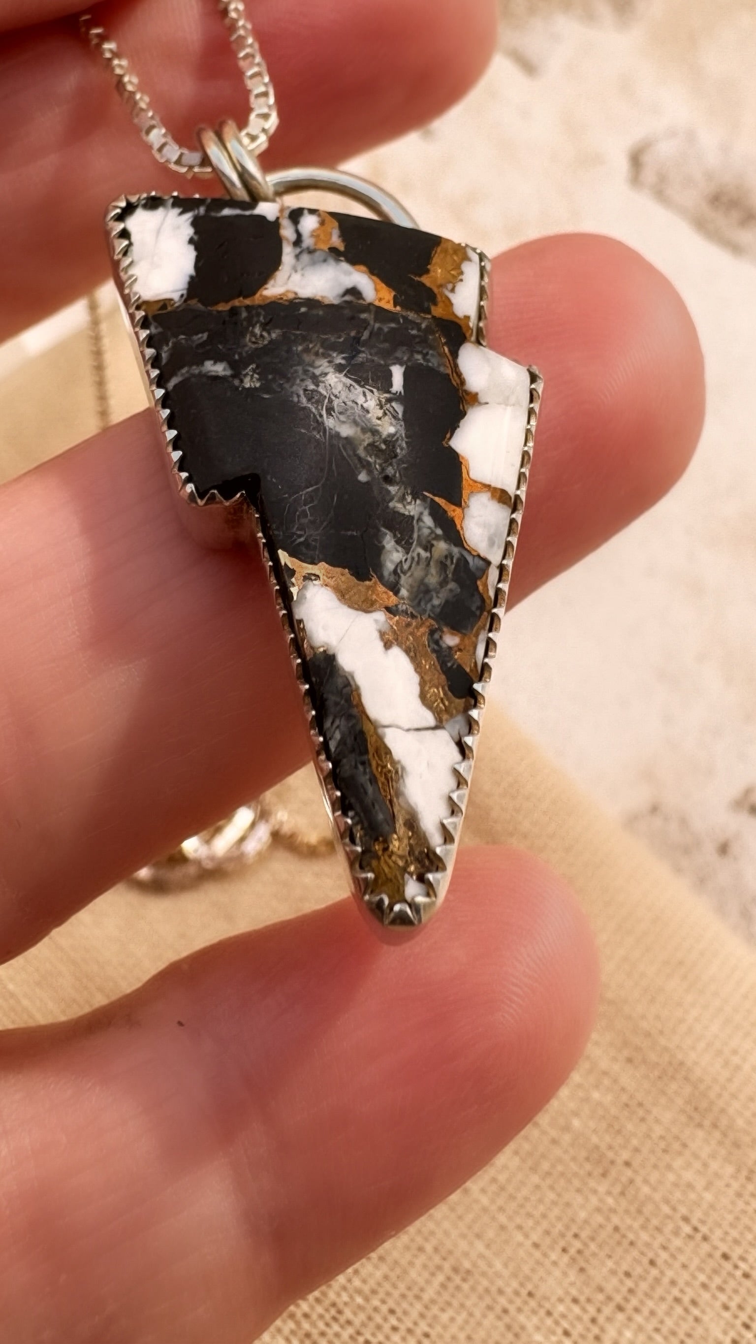 Lightning bolt-shaped pendant held in a hand with a blurred background