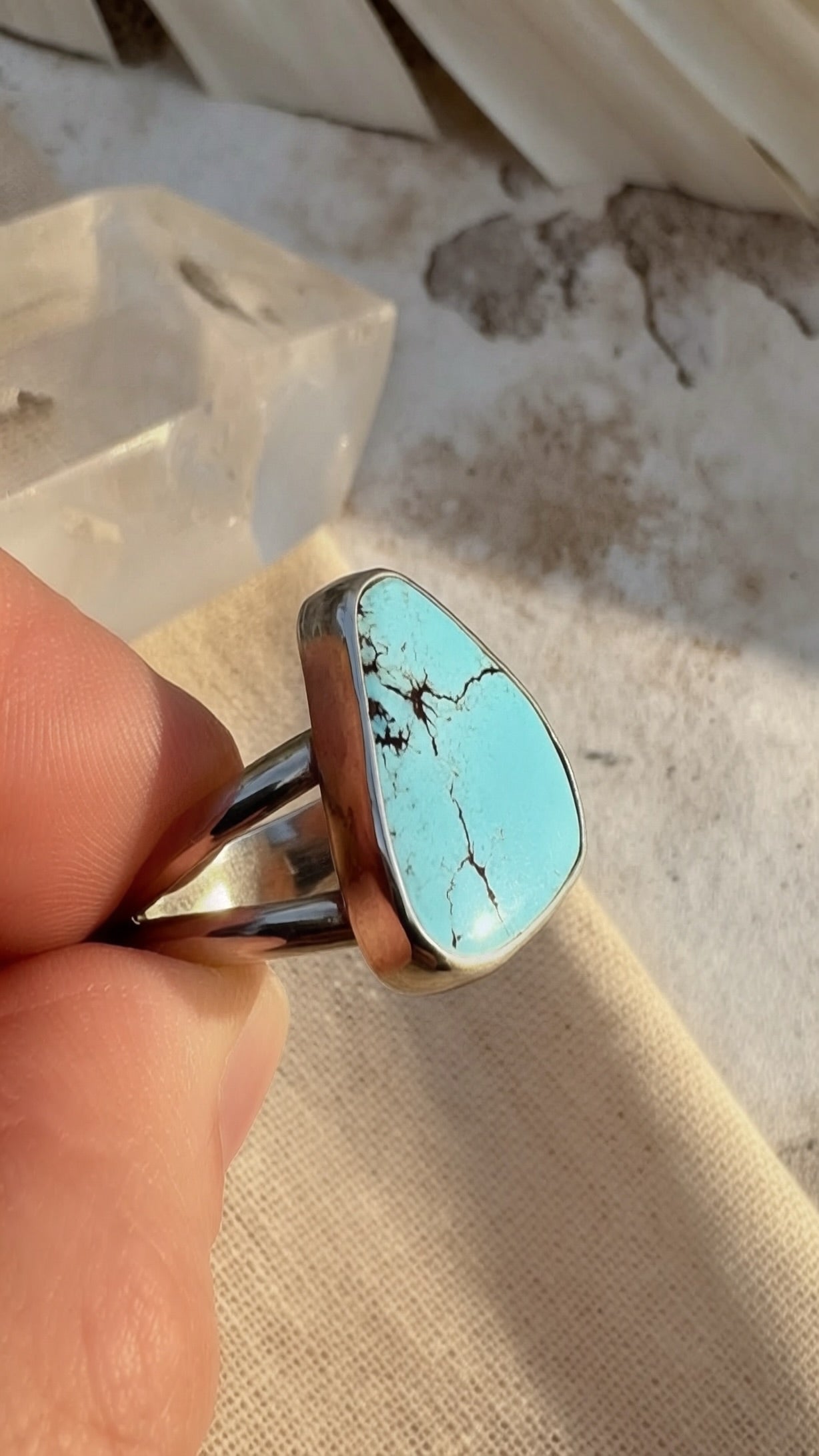 Turquoise stone ring held by a hand on a textured surface