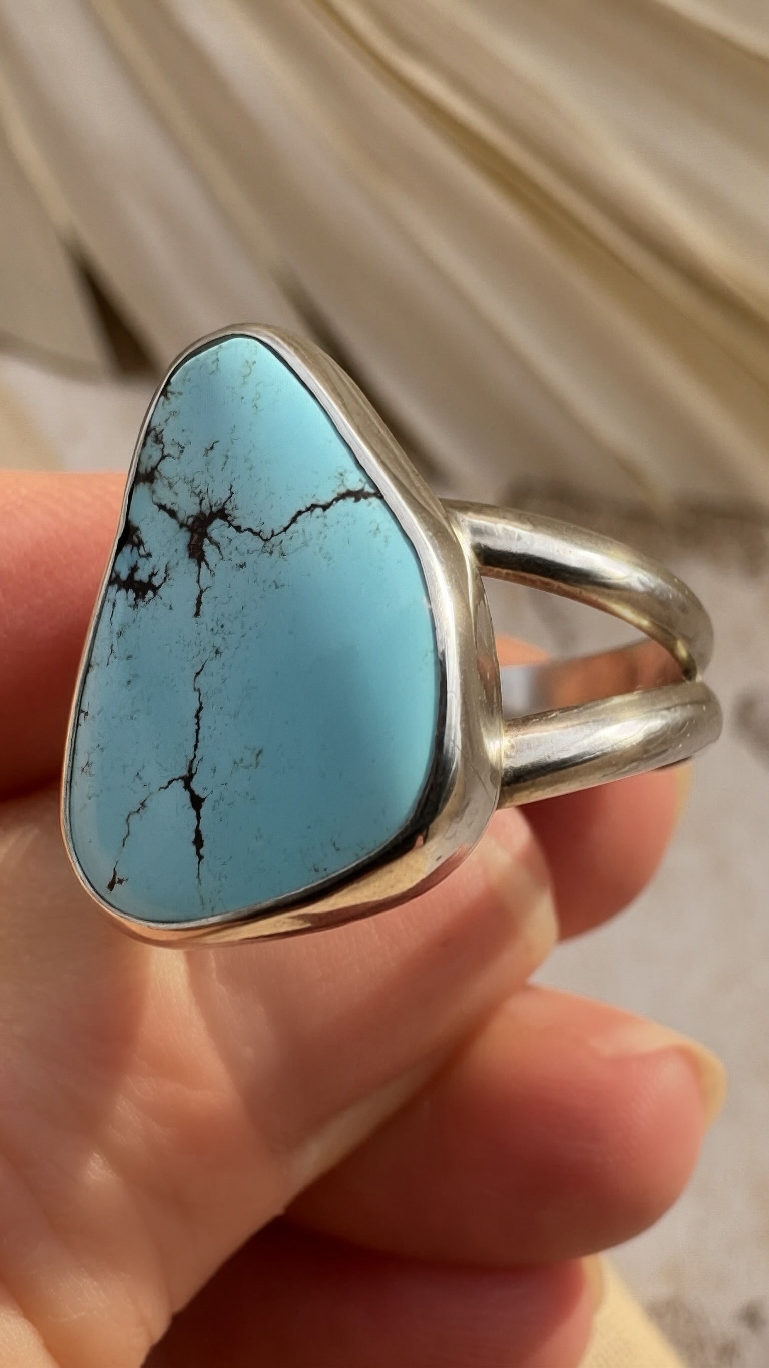 Silver and Turquoise ring with silver band held in a hand against a neutral background