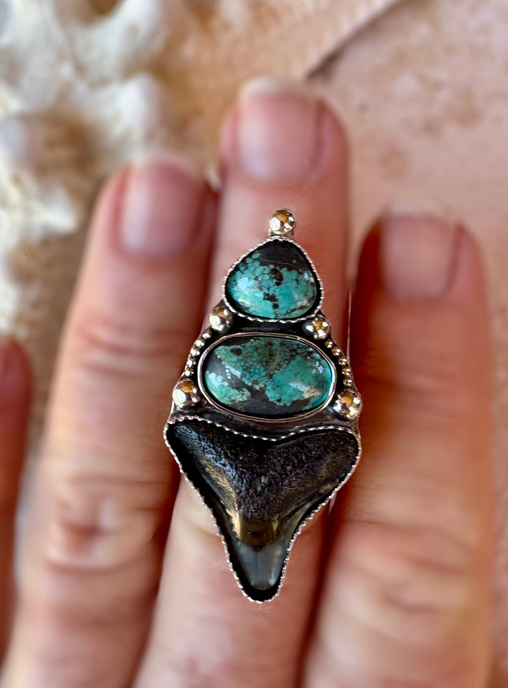 Turquoise, shark tooth and silver ring on a finger with a neutral background