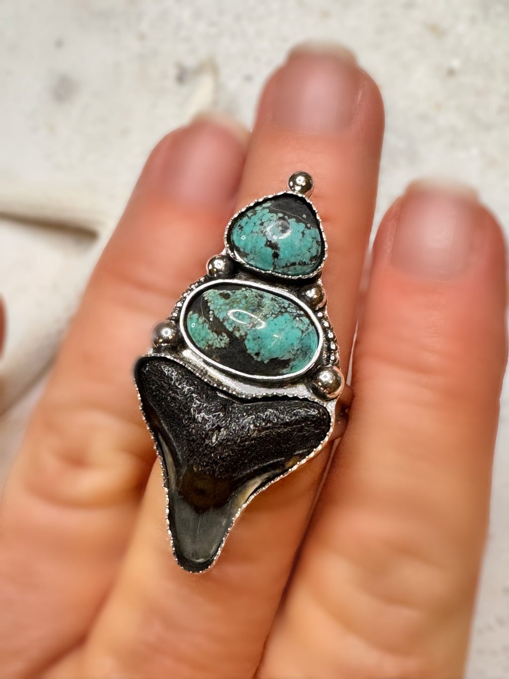 Turquoise, shark tooth and silver ring on a finger with a neutral background