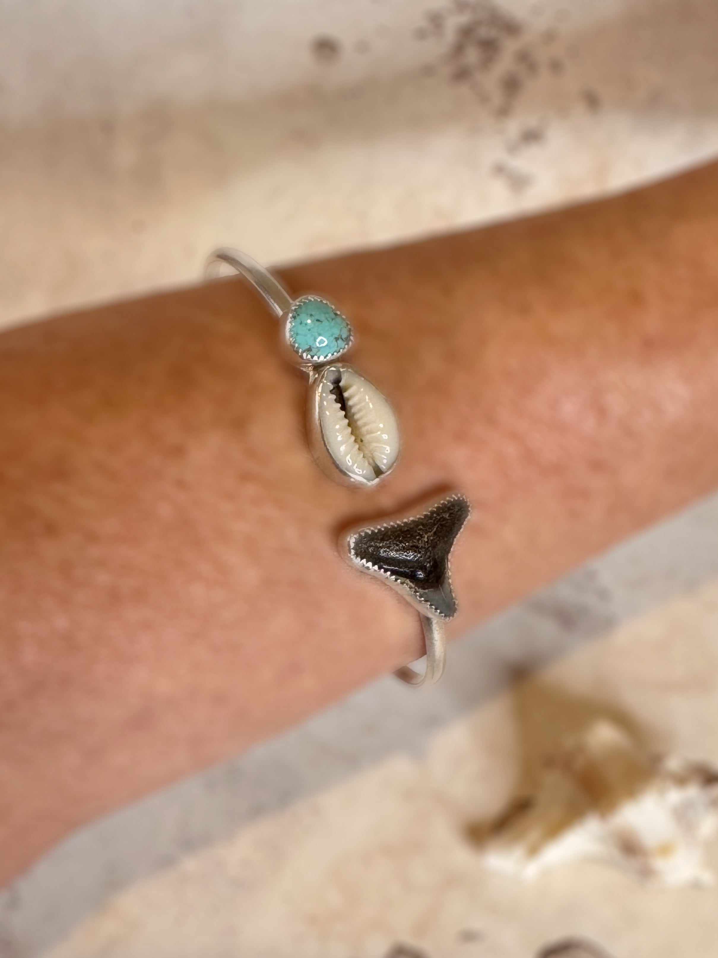 Silver bracelet with turquoise stone and shell on a wrist against a neutral background