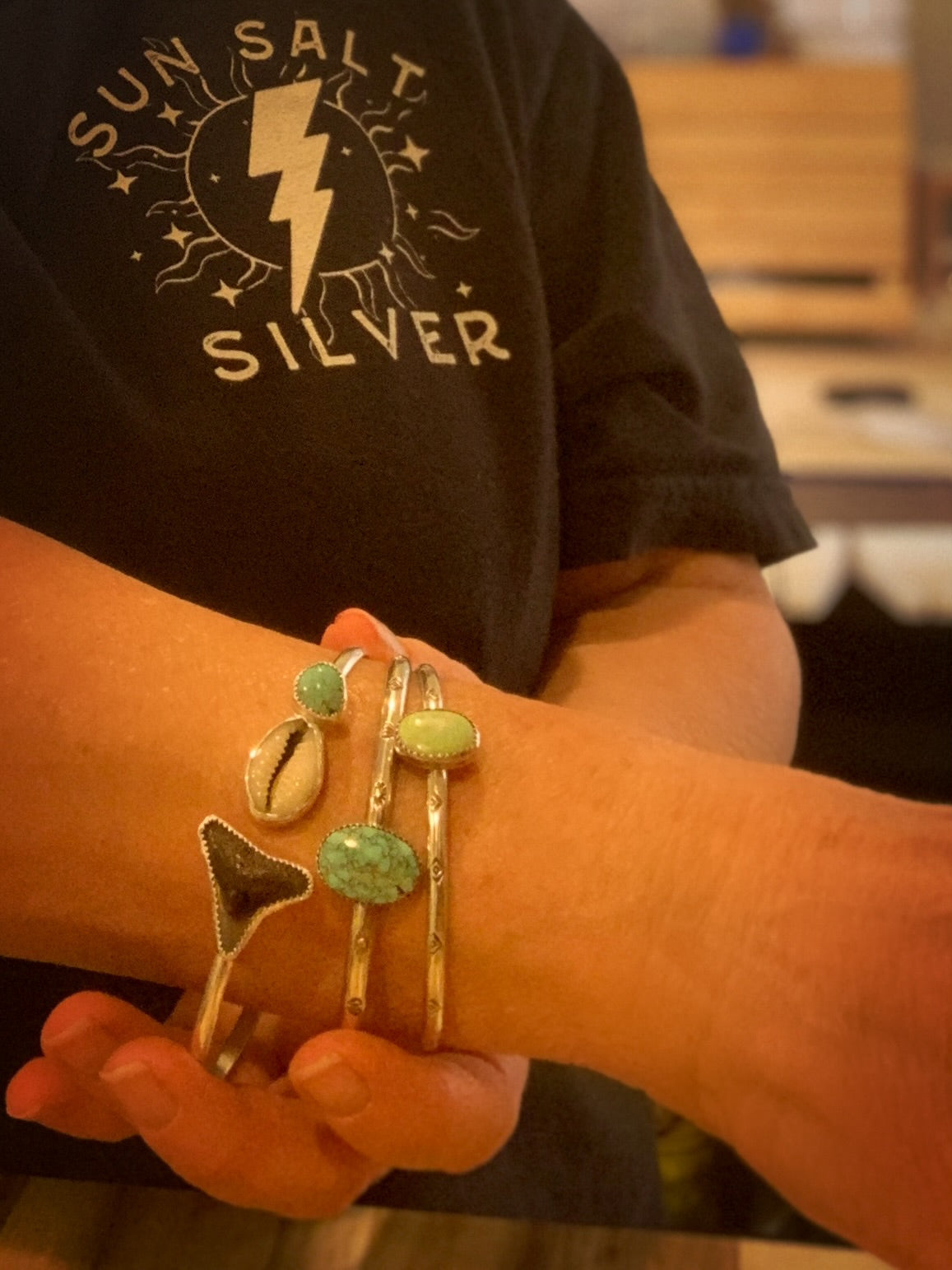 Person wearing multiple bracelets on a blurred background with 'Sun Salt Silver' branding.