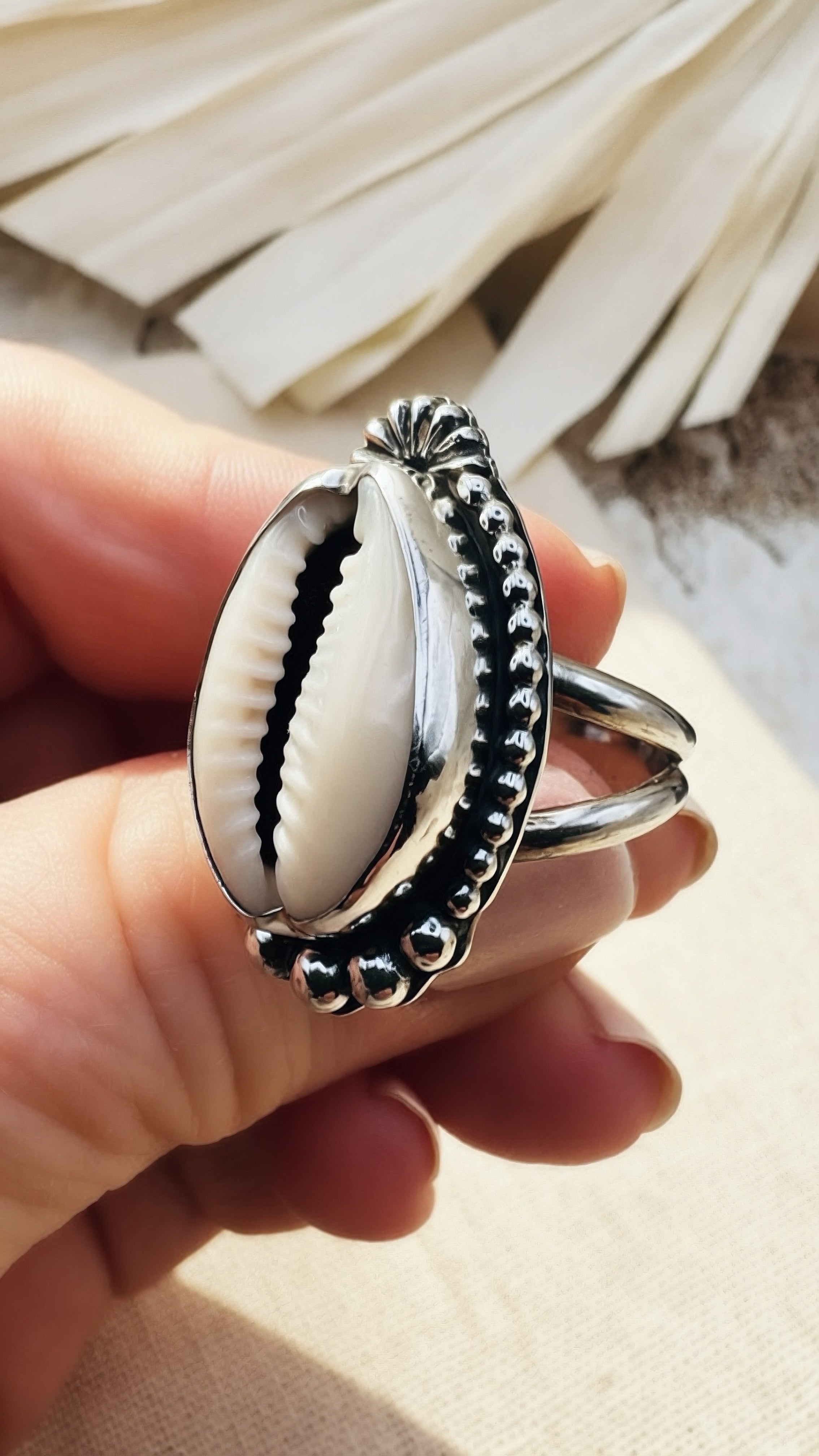 Silver ring with a shell design held in a hand against a neutral background