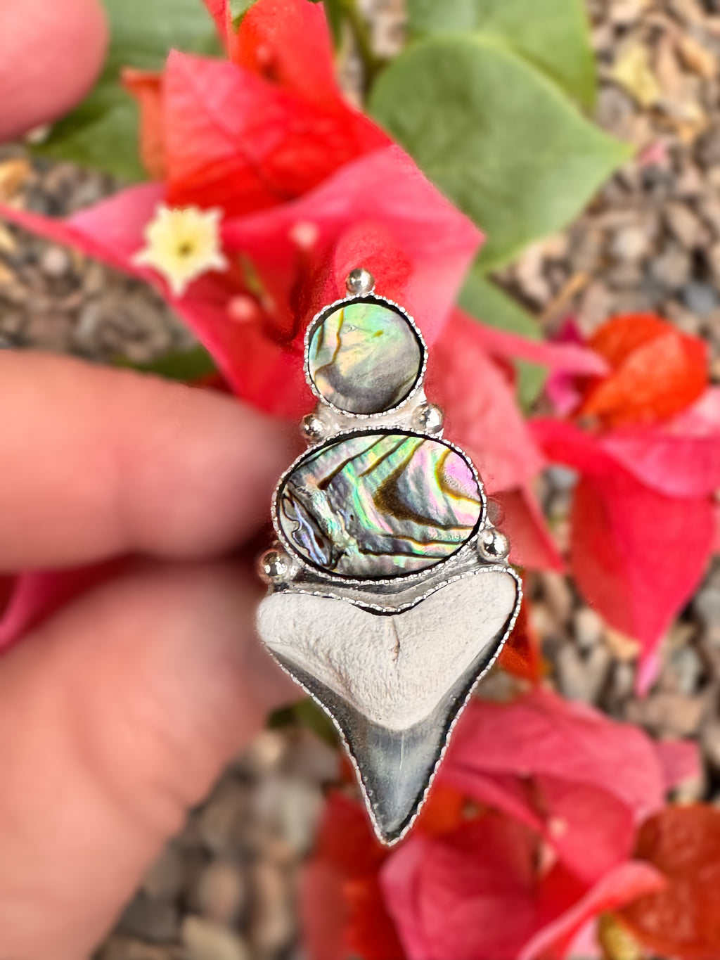 Silver ring with abalone shell and a shark tooth on a finger against a bougainvillea background