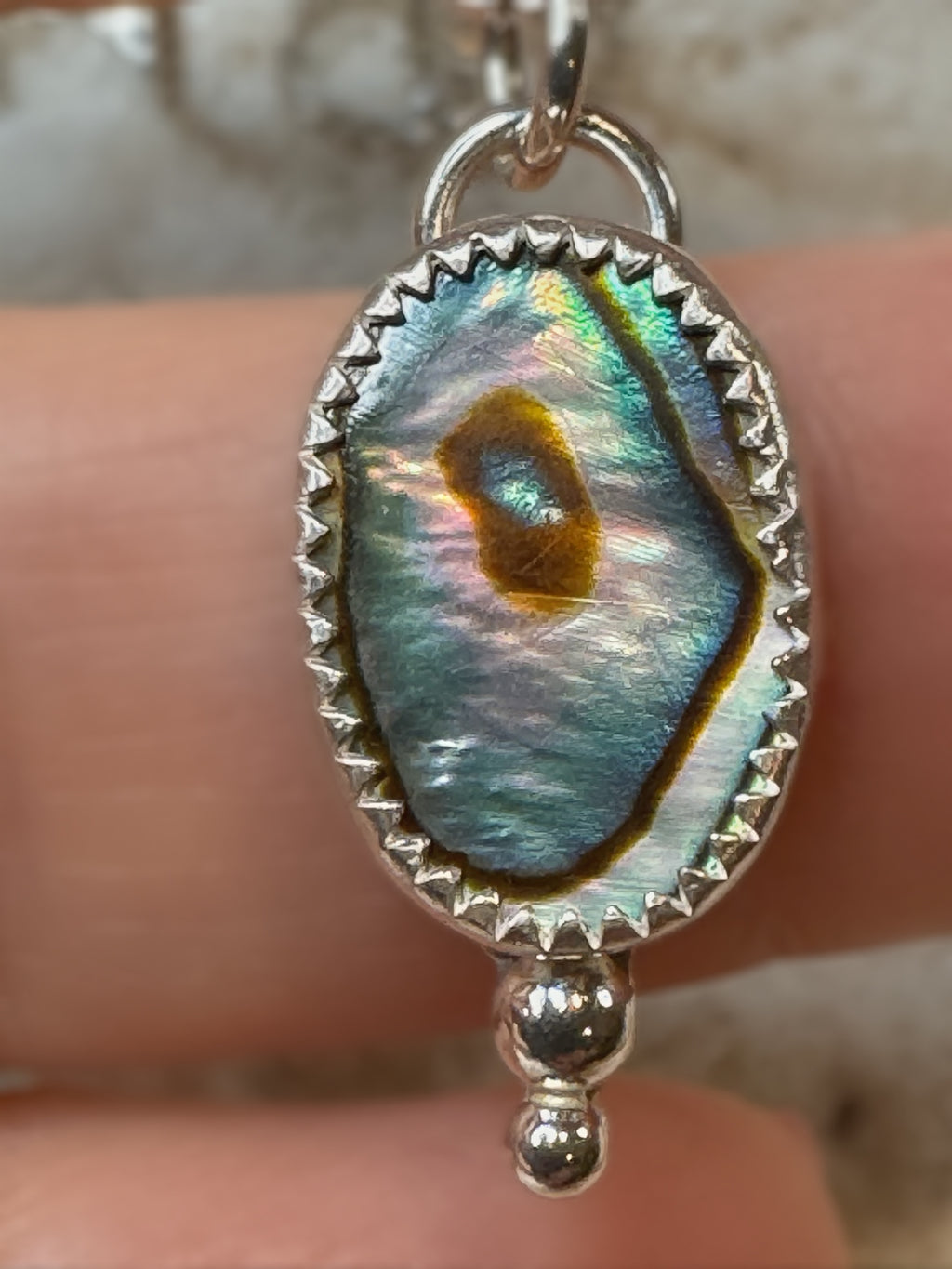 Pendant with abalone shell design held between fingers