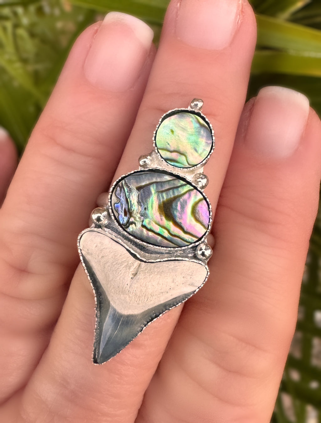 Silver ring with abalone shell on a finger against a natural background