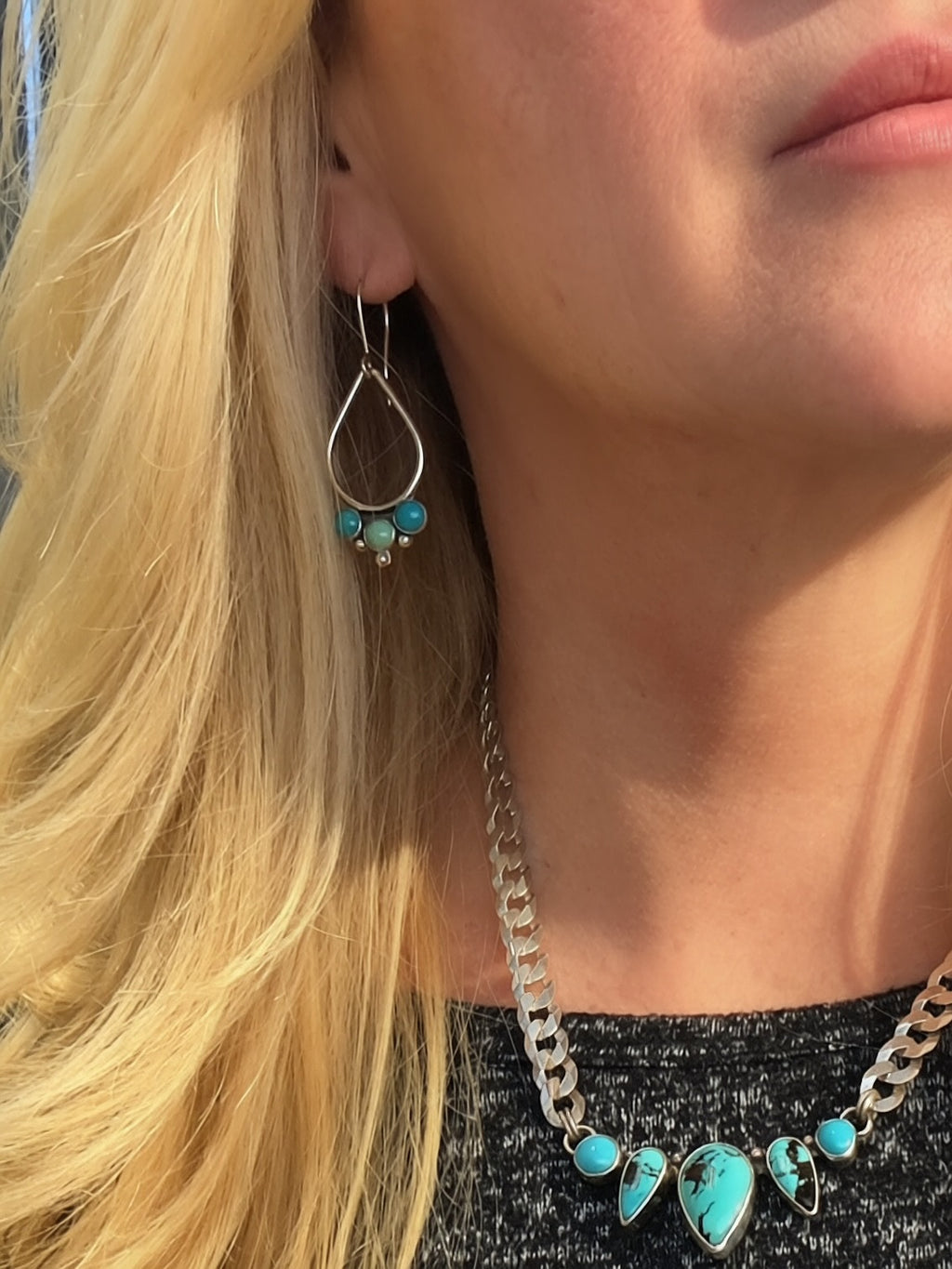 A close-up of a woman wearing a silver-toned necklace and matching drop earrings with turquoise-colored stones.