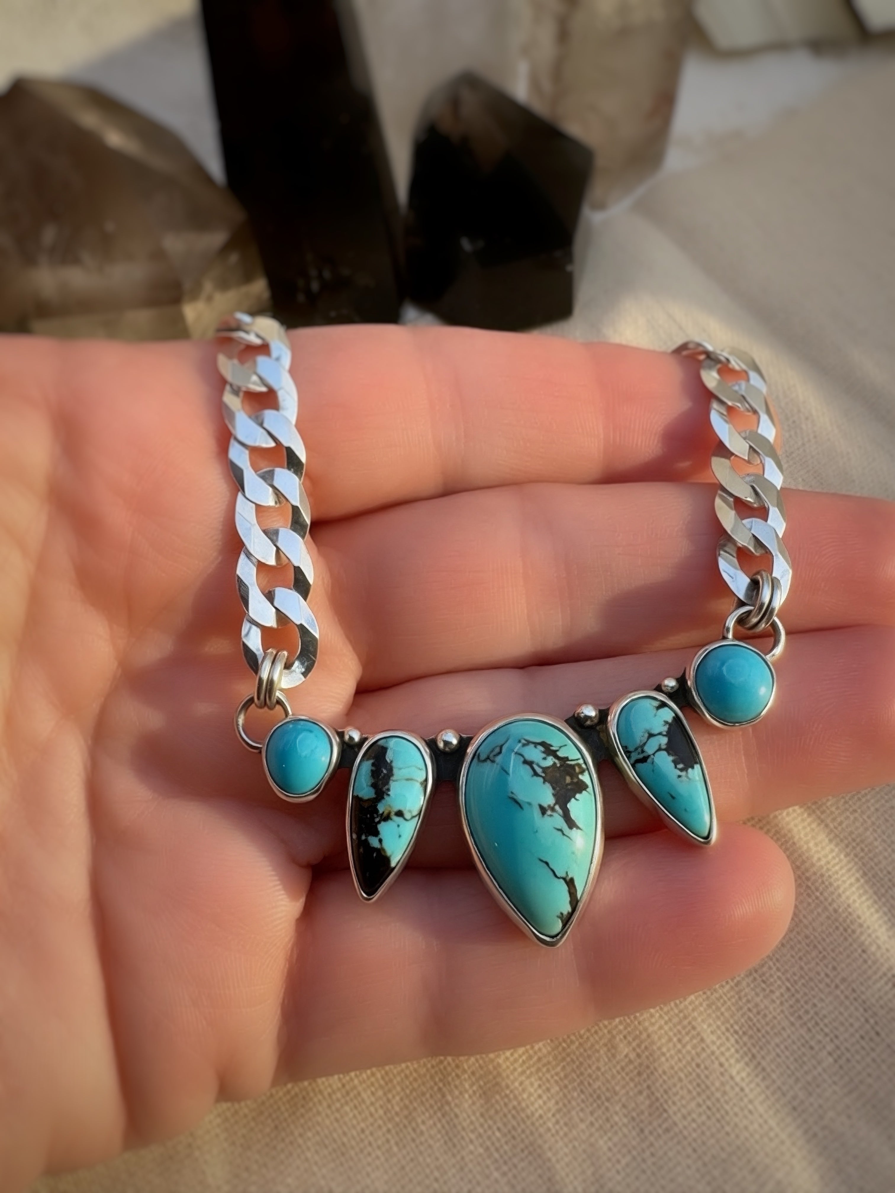 Turquoise stone necklace with silver curb chain on a hand with a blurred background