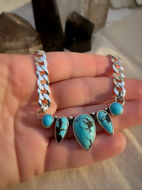 Turquoise stone necklace with silver curb chain on a hand with a blurred background