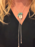 Handmade bolo necklace featuring cowrie shell, Fox turquoise, and white topaz in sterling silver, called Tidebearer.