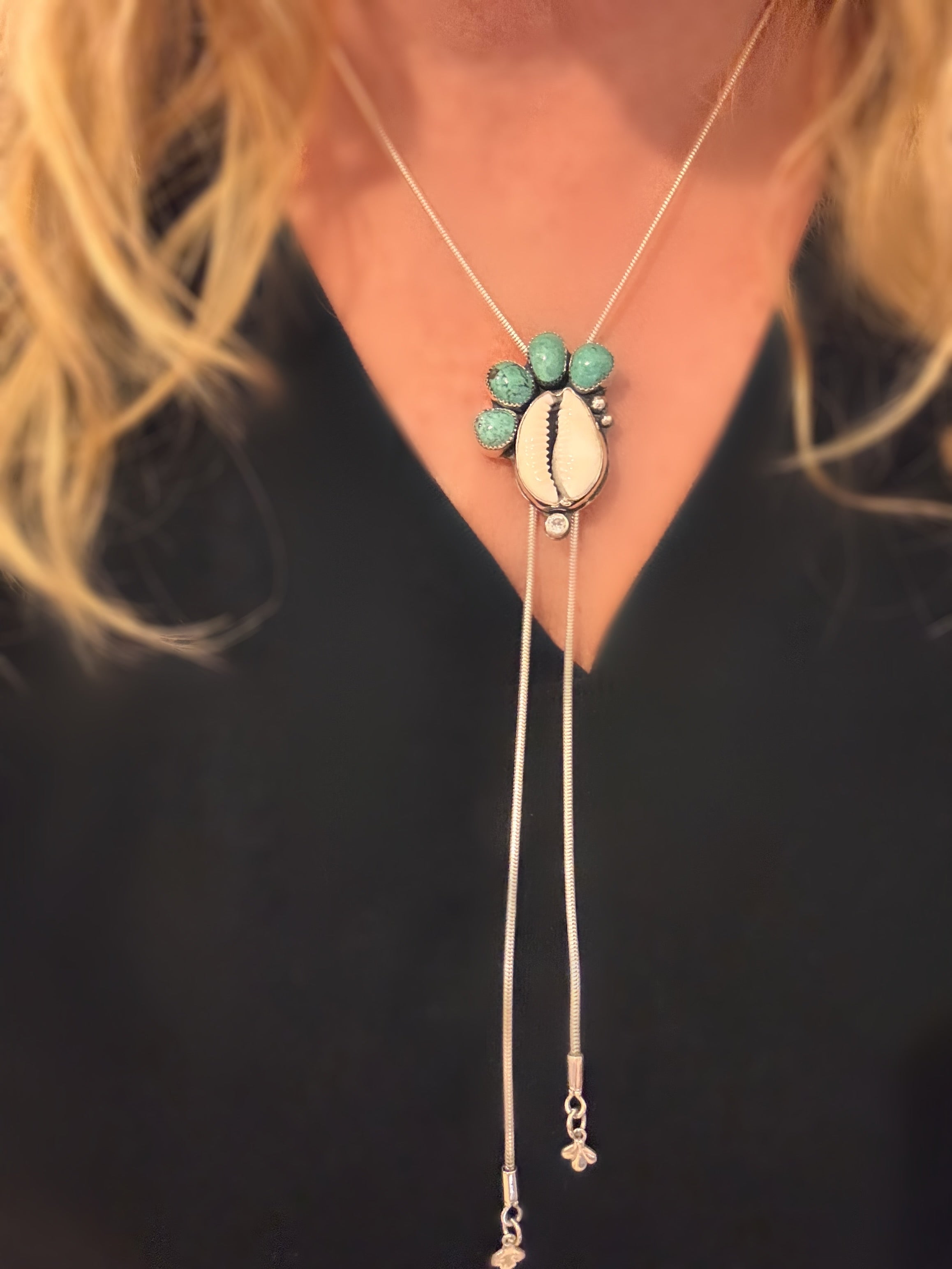 Handmade bolo necklace featuring cowrie shell, Fox turquoise, and white topaz in sterling silver, called Tidebearer.