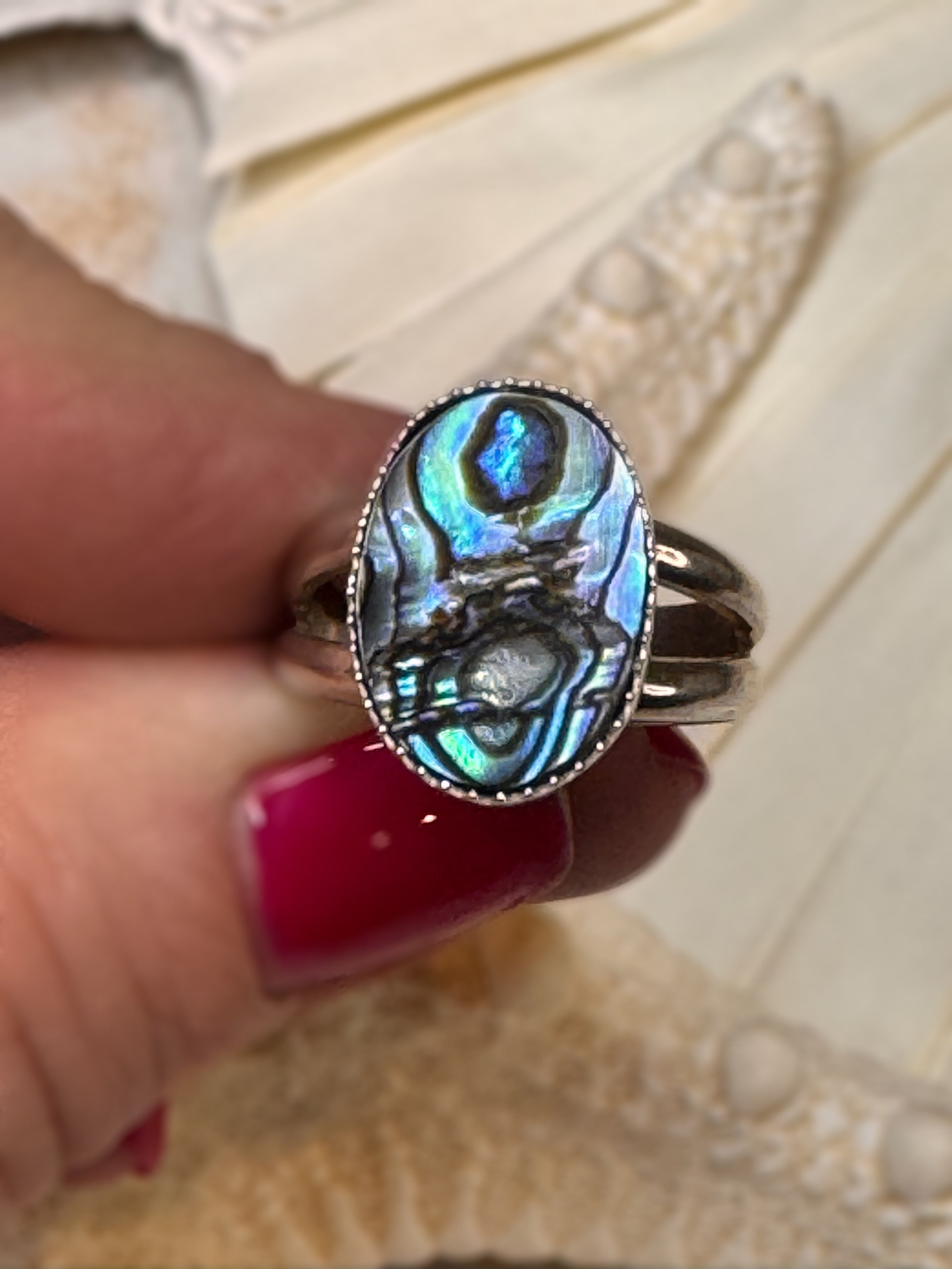 Handmade silver ring with an oval abalone shell, shimmering in shades of teal, blue, and violet.