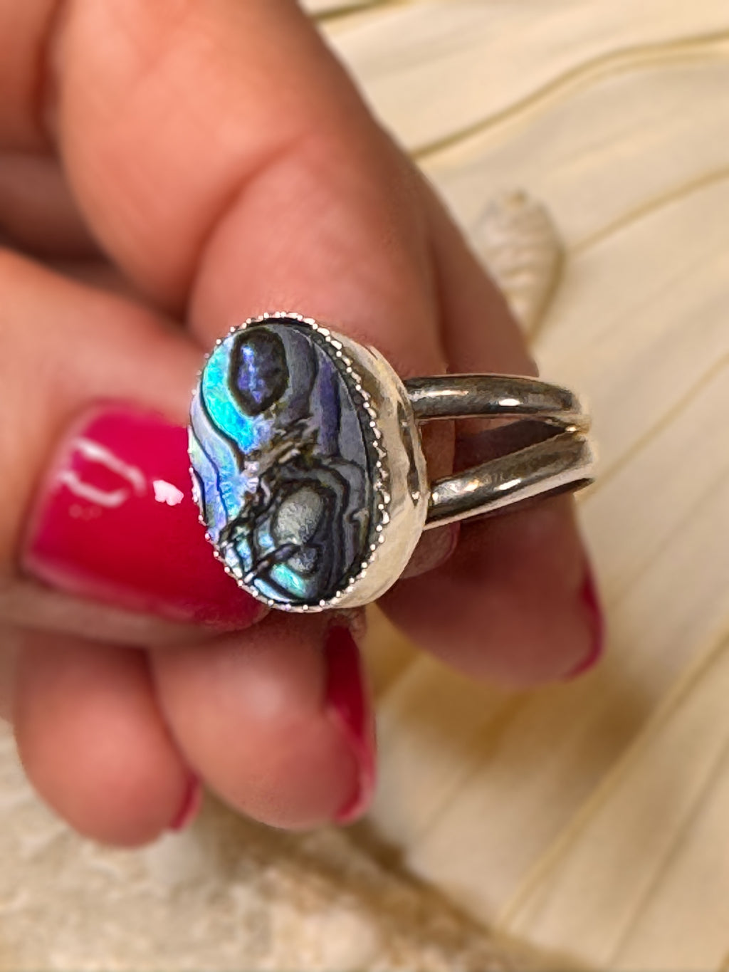 Abalone shell ring photographed from the side, showing its silver bezel and luminous ocean-inspired colors.