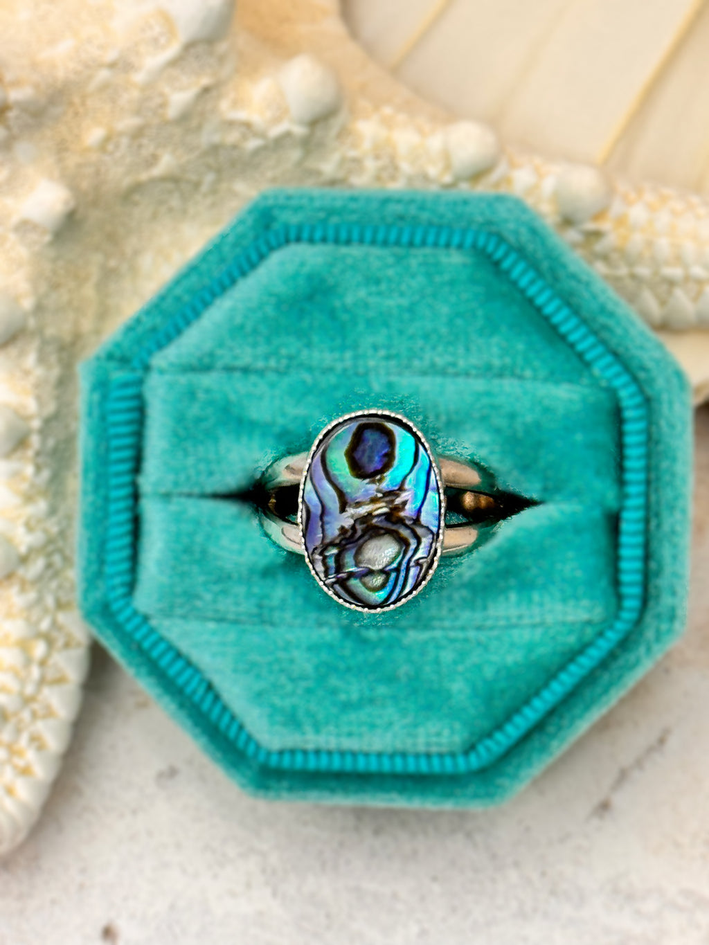 Handmade silver ring with an oval abalone shell, shimmering in shades of teal, blue, and violet.
