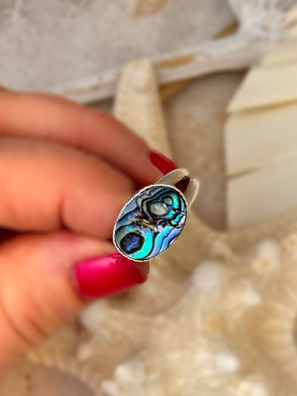 Close-up of a handcrafted abalone shell ring with iridescent blue and green hues, set in fine and sterling silver on a split shank band.