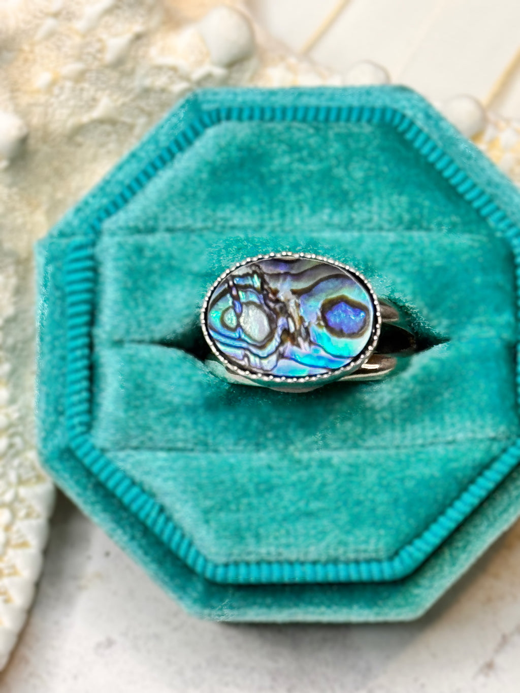 Handmade silver ring with an oval abalone shell, shimmering in shades of teal, blue, and violet.
