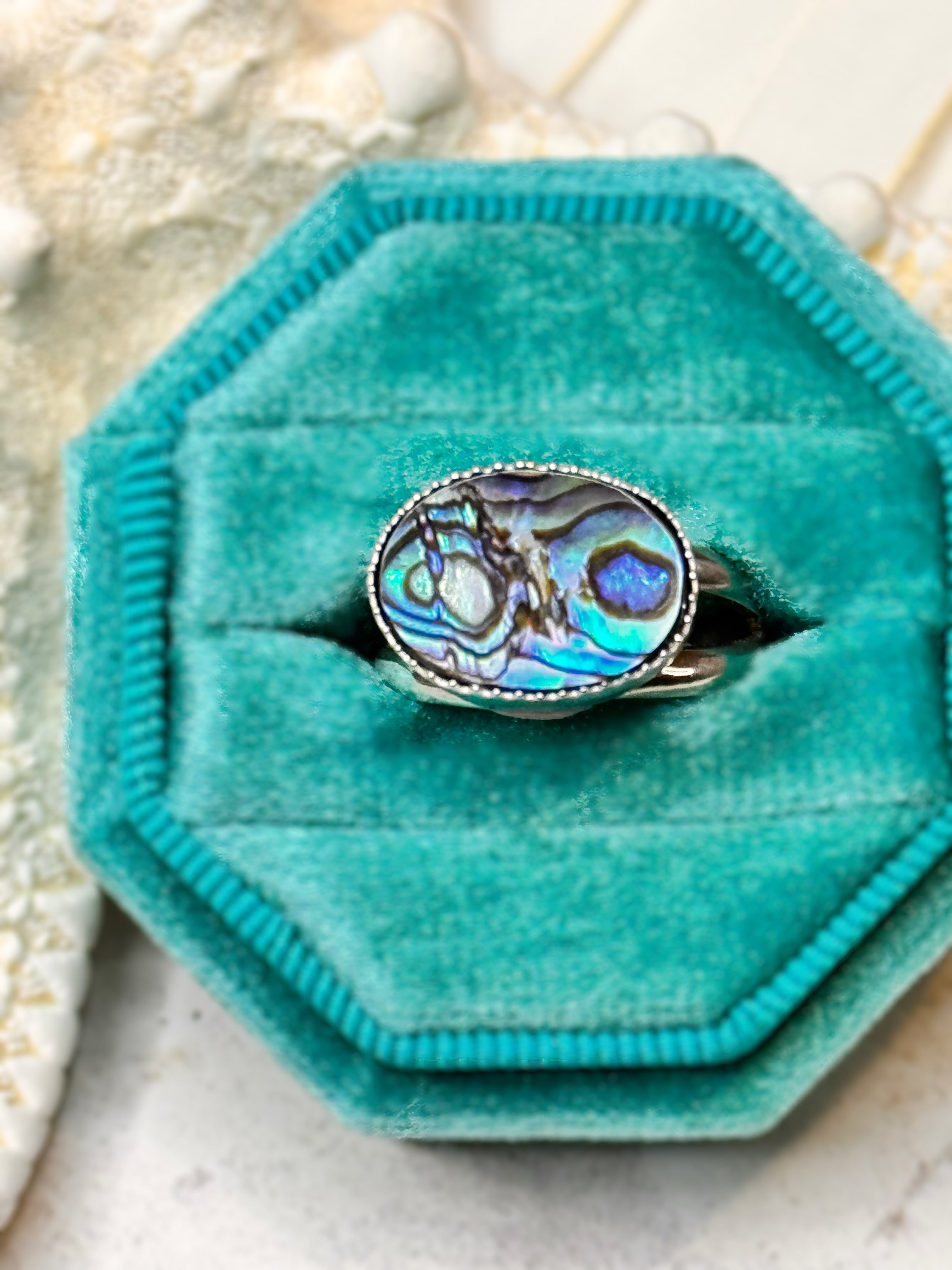 Handmade silver ring with an oval abalone shell, shimmering in shades of teal, blue, and violet.