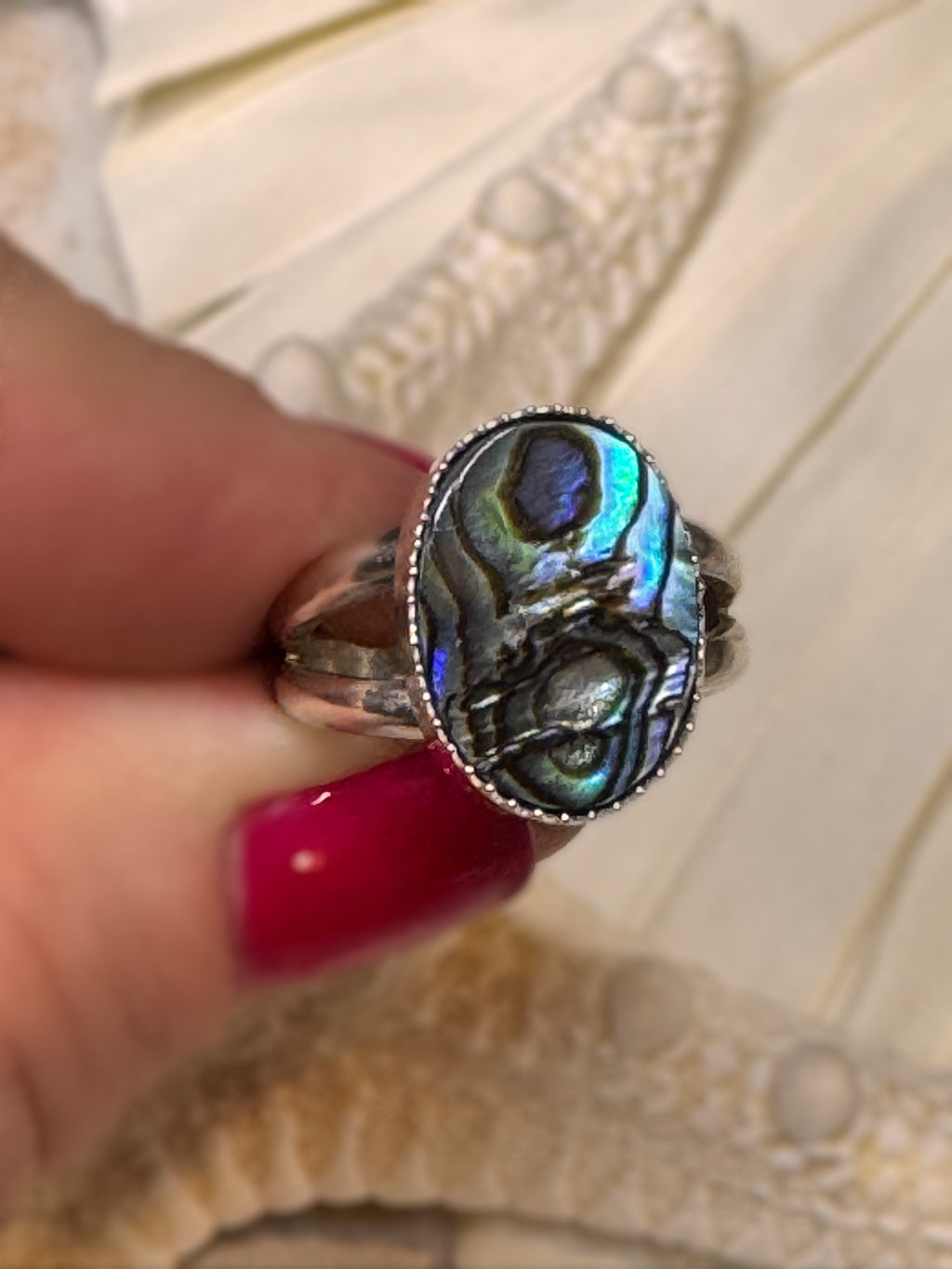 Abalone shell ring photographed from the side, showing its silver bezel and luminous ocean-inspired colors.