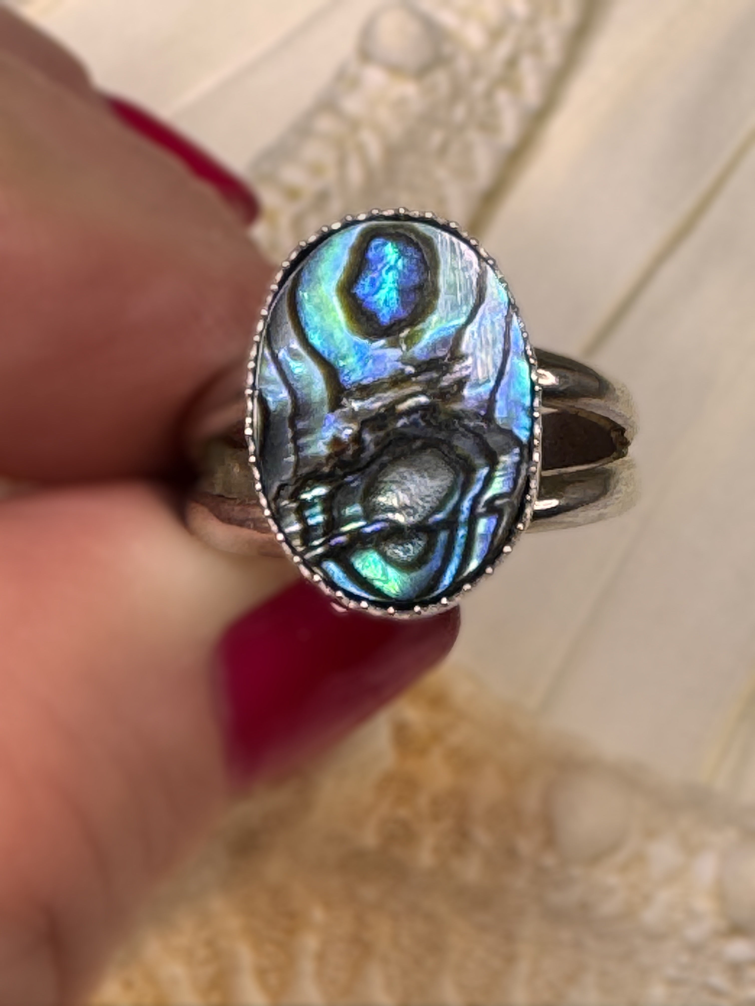 Handmade silver ring with an oval abalone shell, shimmering in shades of teal, blue, and violet.