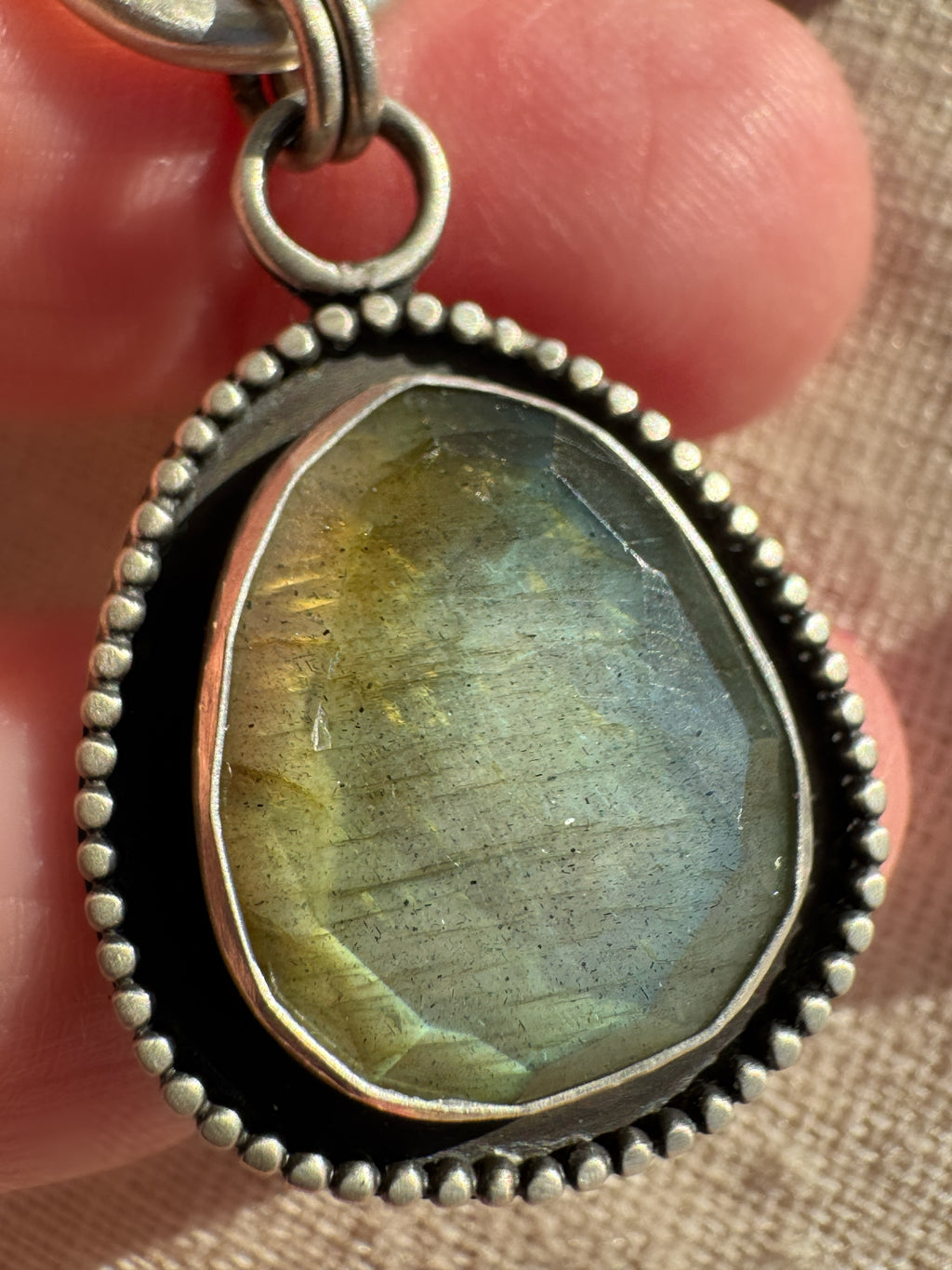 Close-up of the Desert Aurora rose-cut labradorite pendant showing its gold-to-green flash, fine silver bezel and oxidized satin finish.