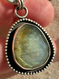 Close-up of the Desert Aurora rose-cut labradorite pendant showing its gold-to-green flash, fine silver bezel and oxidized satin finish.