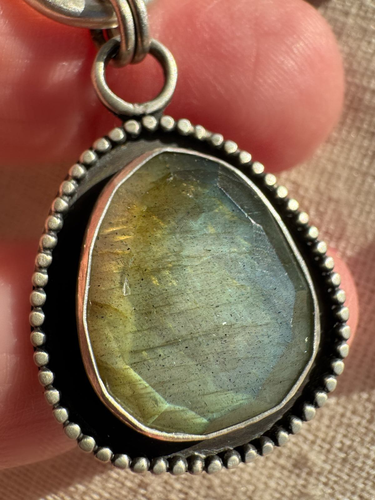 Close-up of the Desert Aurora rose-cut labradorite pendant showing its gold-to-green flash, fine silver bezel and oxidized satin finish.