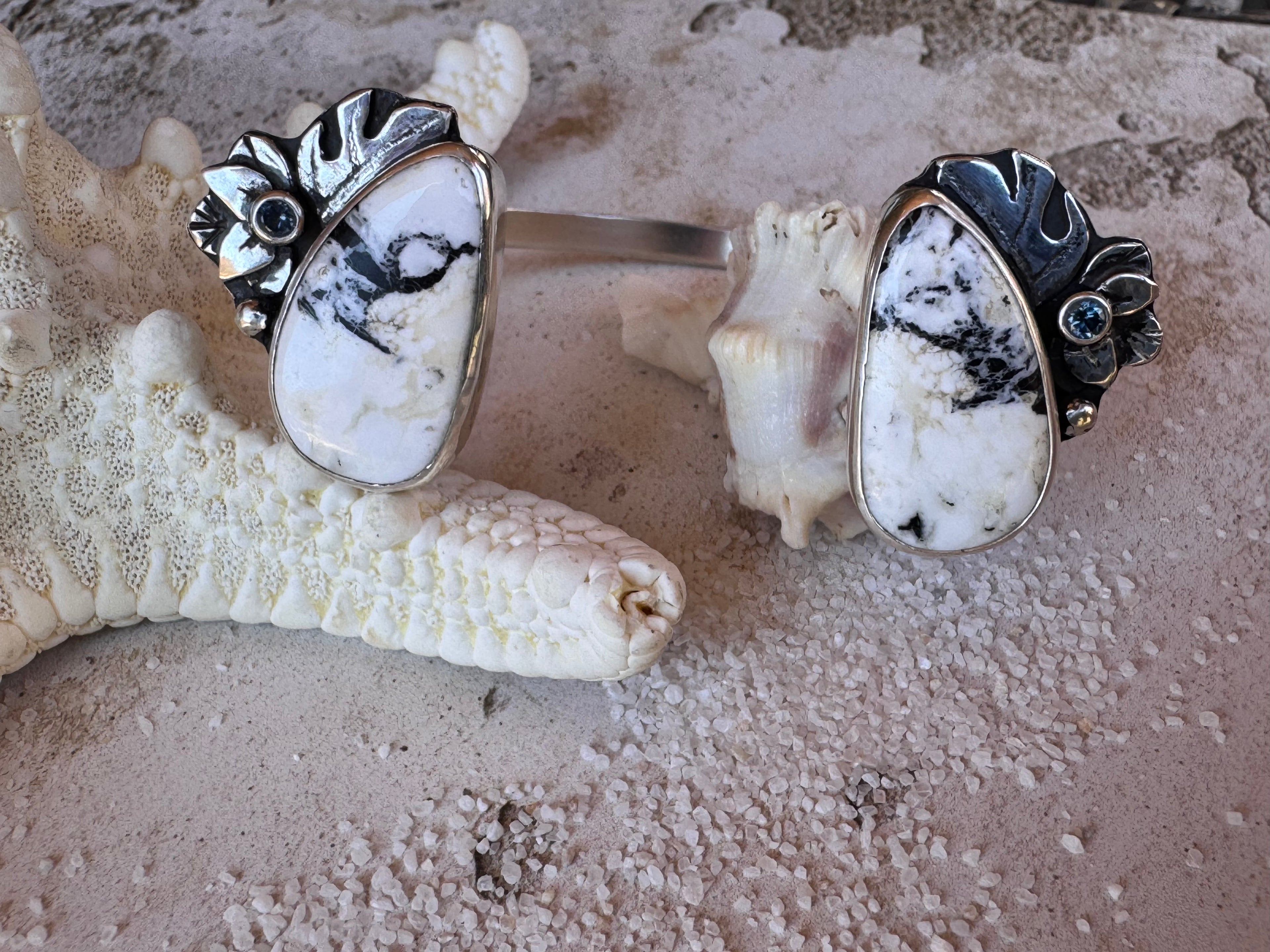 Close-up of a wrist wearing a silver, white buffalo, Montana sapphire and monstera leaf cuff on a textured surface.