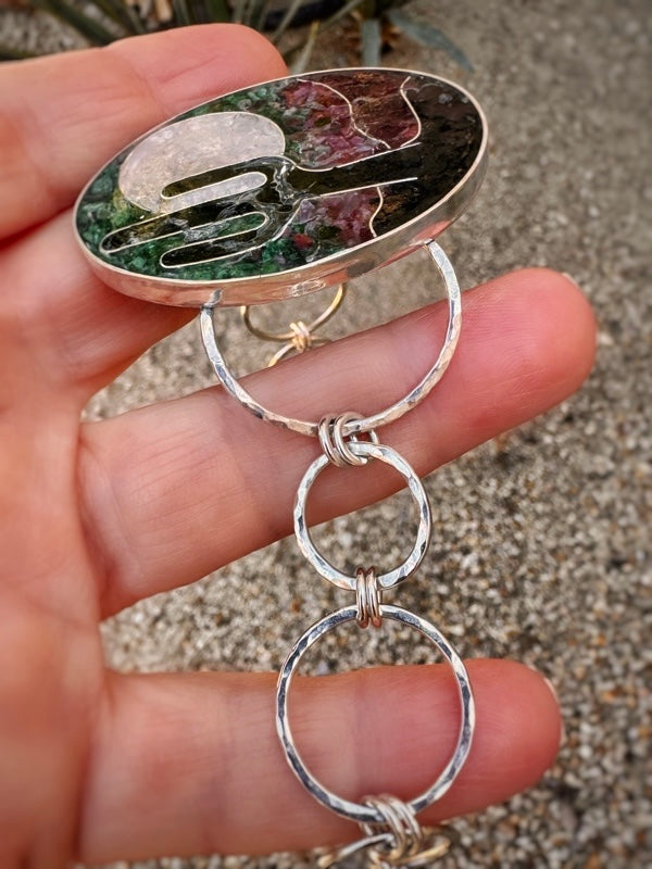 Silver bracelet with a hand design held in a hand against a gravel background